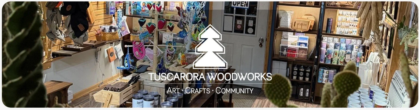 Inside Tuscarora WoodWorks' gift shop with wooden shelves and displays of handmade jewelry, candles, mugs, and various art crafts, with a sign that reads 'Tuscarora Woodworks - Art, Crafts, Community'.