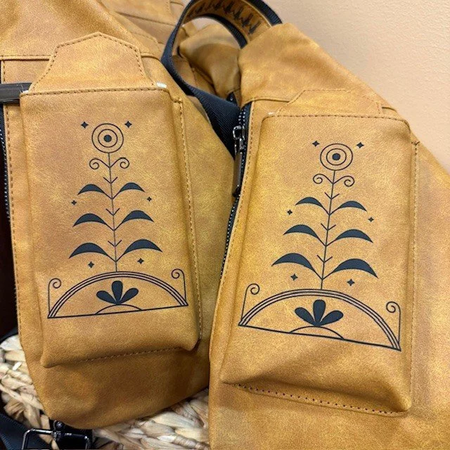 Two tan fabric pouches with black line art floral designs, attached to a tan bag with a zipper and some black straps.