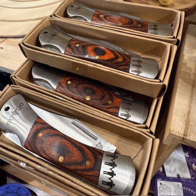 Four boxed folding pocket knives with wooden handles displayed inside cardboard boxes.