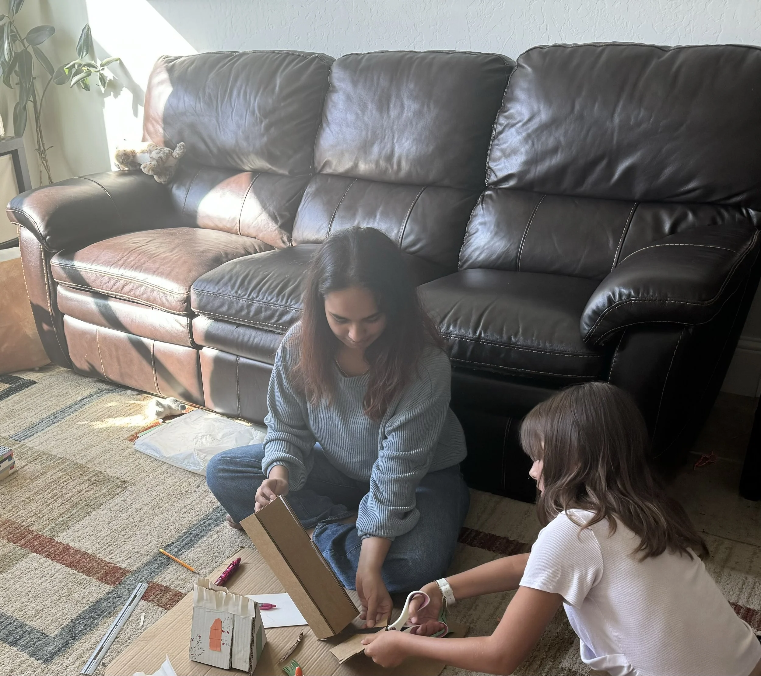 A female scientist in a white lab coat explains a science experiment with a dropper to a group of six children standing in front of her in a science museum or classroom. The children are attentively watching her demonstration around a white table with scientific equipment, including bottles and a glass jar.