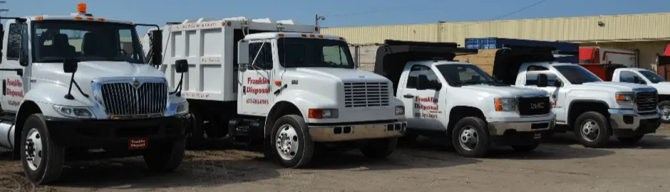 Four utility trucks parked in a lot in front of a yellow building with a blue sky overhead.