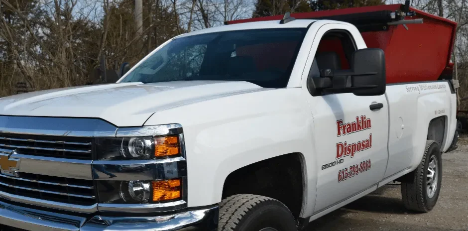 White pickup truck with a red disposal bed, company logo, and contact information, parked outdoors with trees in the background.