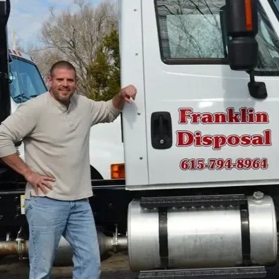 Man standing next to a white Franklin Disposal truck, smiling, with trees and a clear sky in the background.