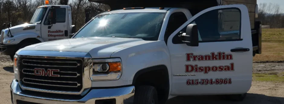 A white GMC disposal truck with 'Franklin Disposal' written on the door and a phone number, parked outdoors with another similar truck in the background.
