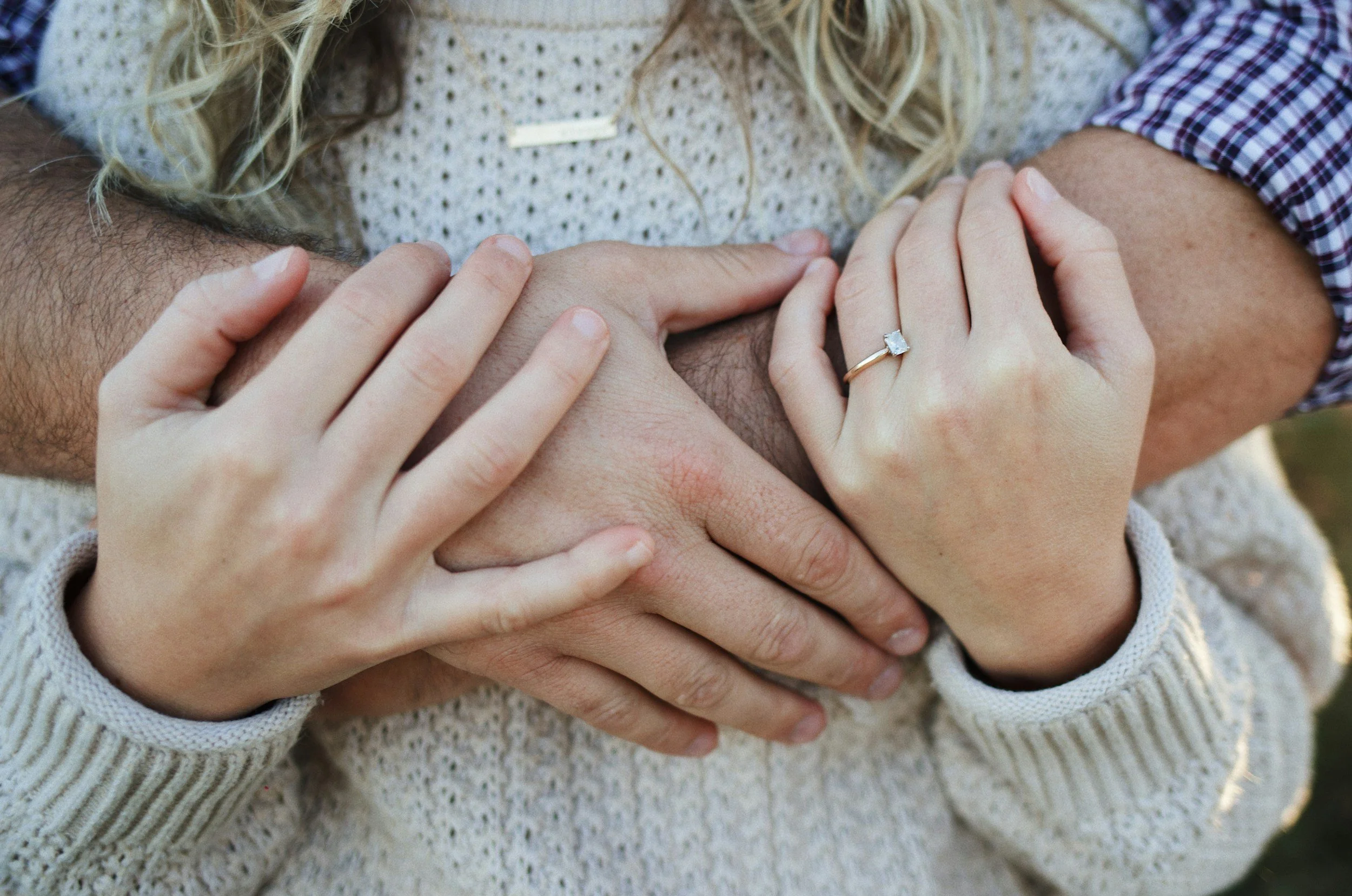 Close-up of hands with one person wearing a ring, gently holding another person's knee.