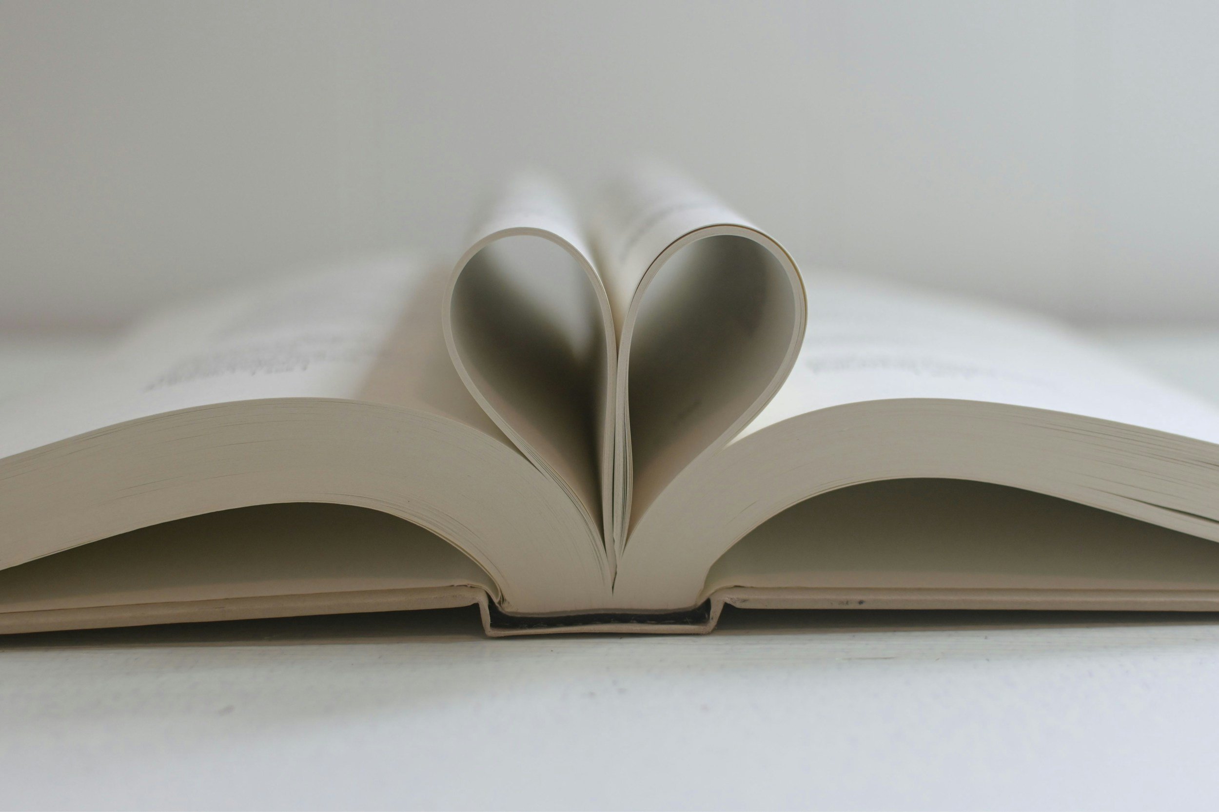 An open book with pages folded into a heart shape in the center.