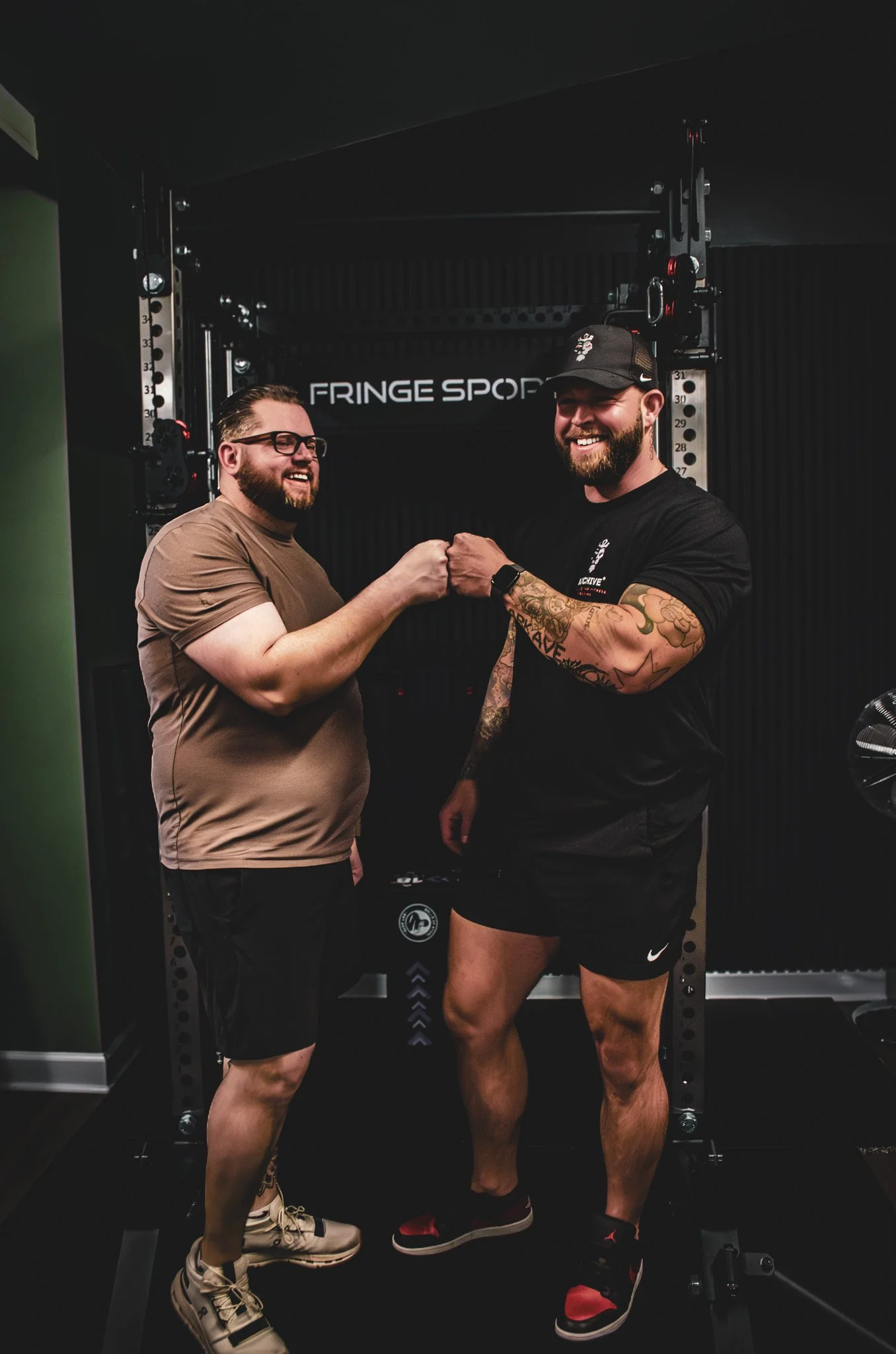 Personal trainer and client fist bumping inside a gym with strength equipment in the background.