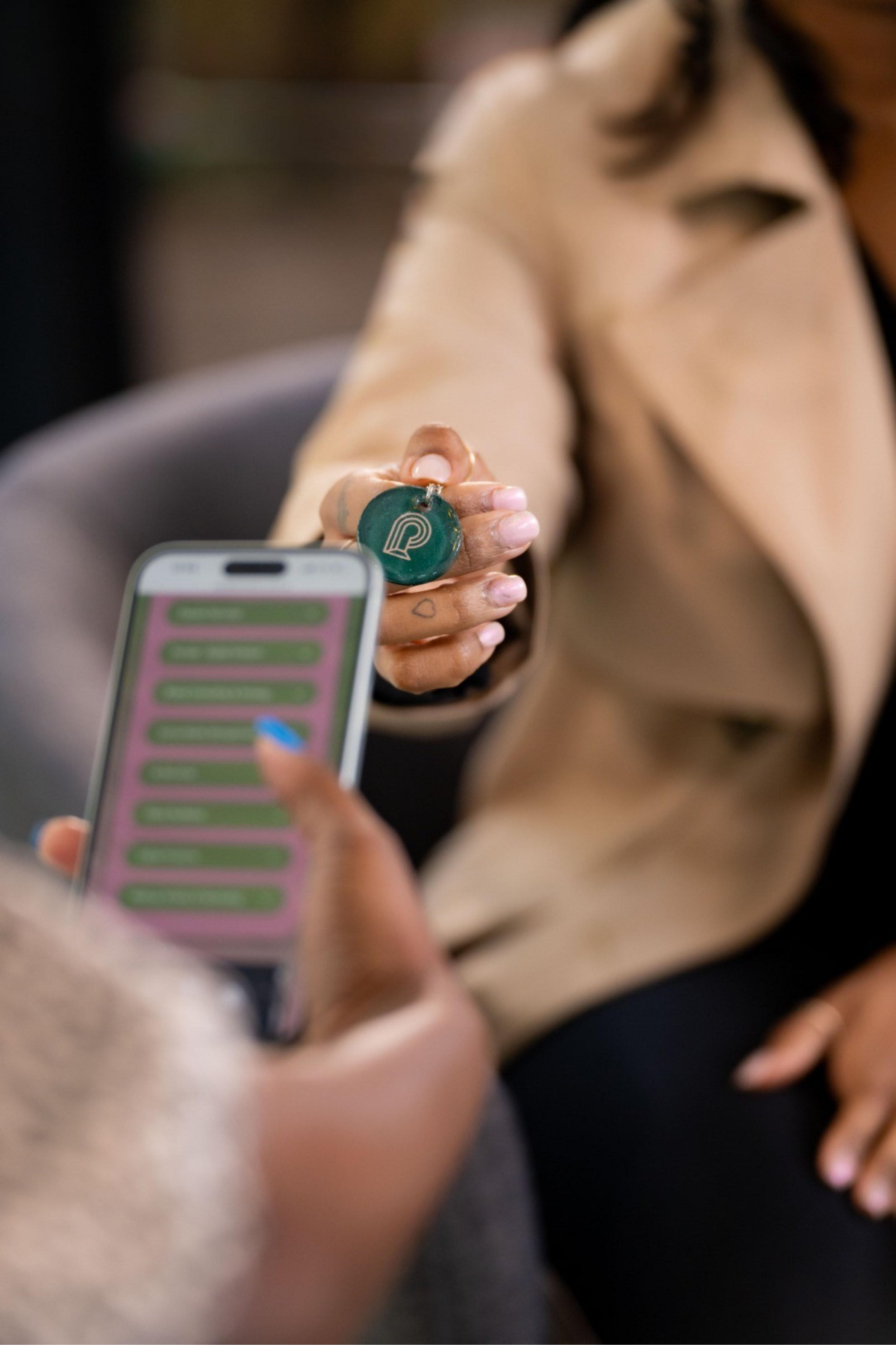 A person holding a green token with a white logo and a keychain, while a phone with a pink and green screen is in the foreground.