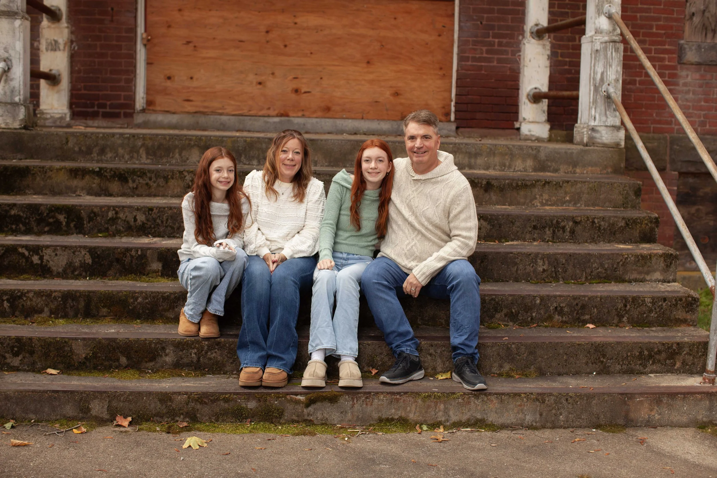 Family of four sitting on outdoor set of stairs in front of a brick building, smiling at the camera.
