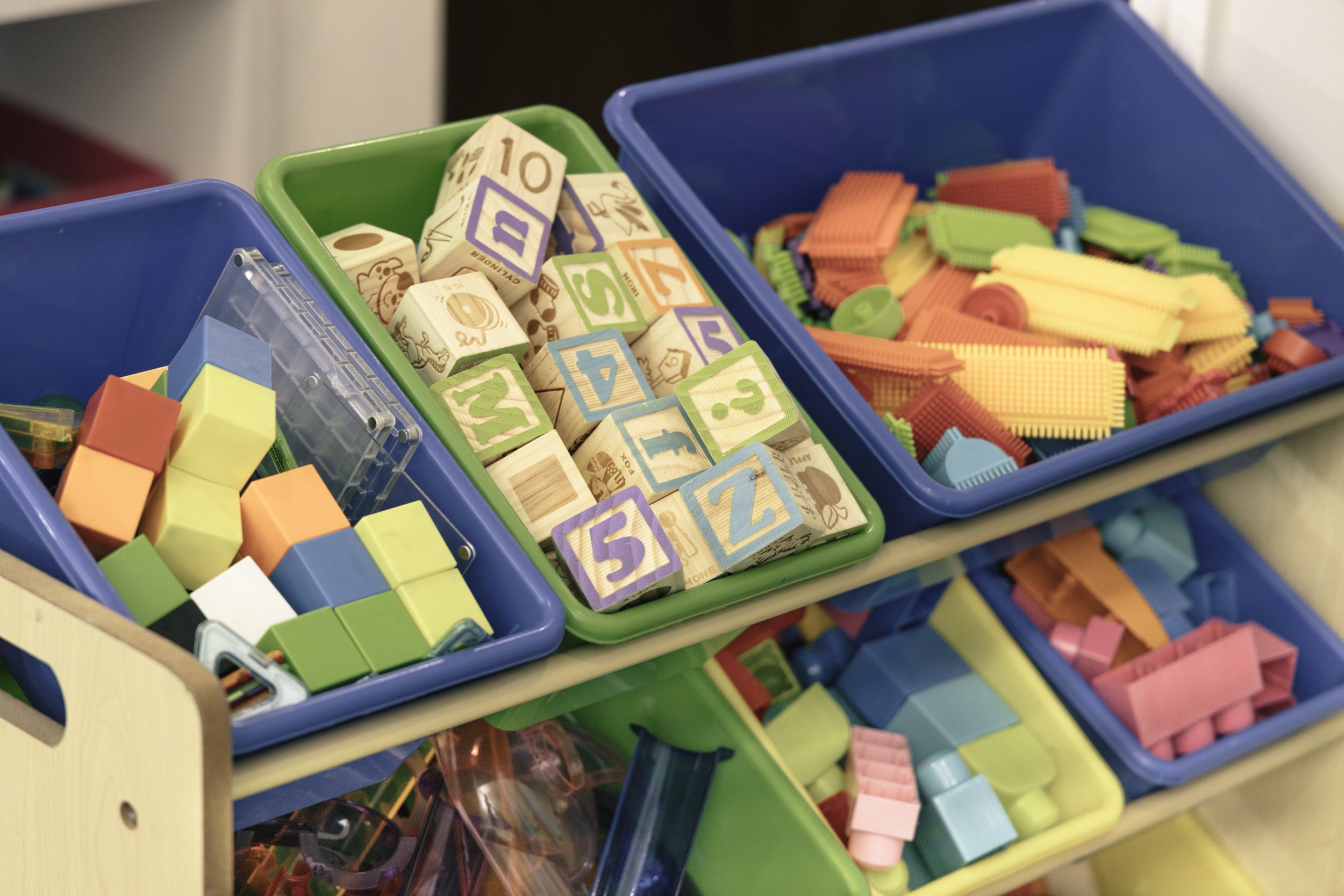 Colorful plastic building blocks and wooden letter blocks in trays, used for children's play and learning.