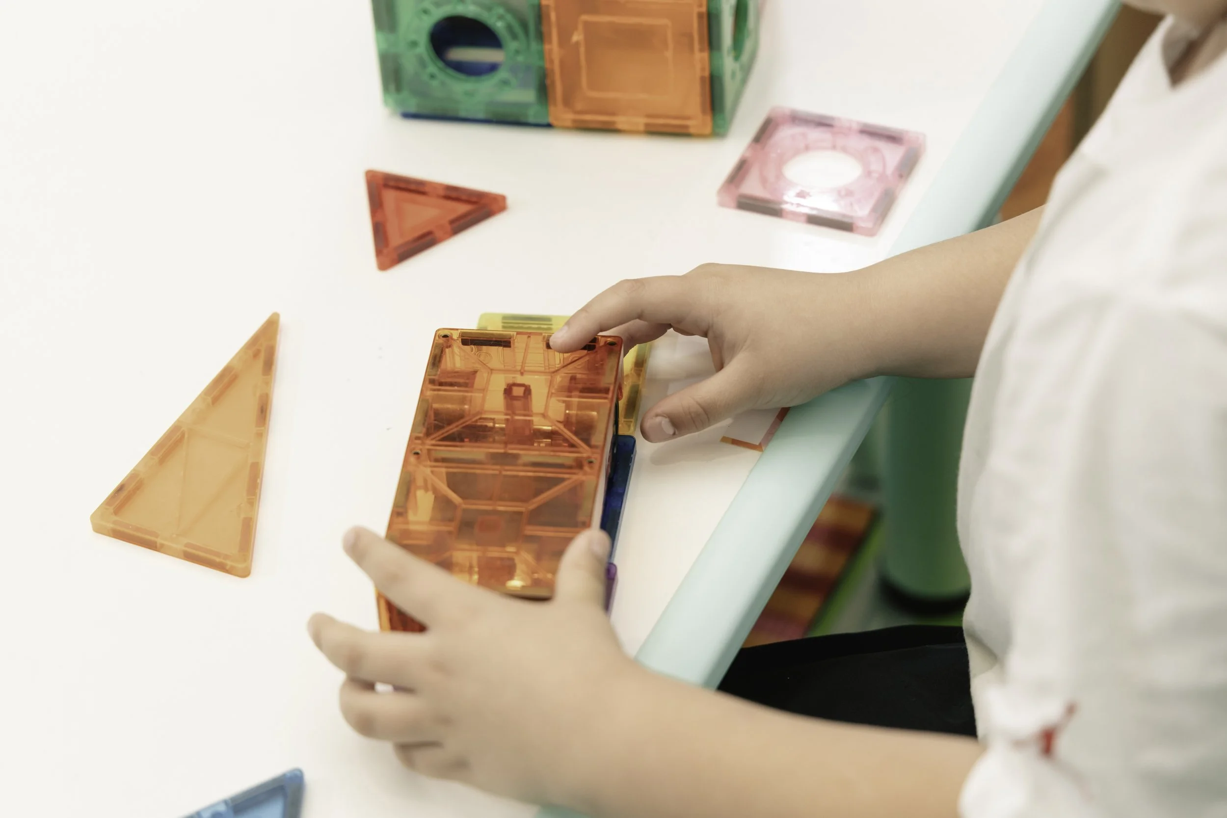 Child playing with colorful magnetic building blocks on a white table.