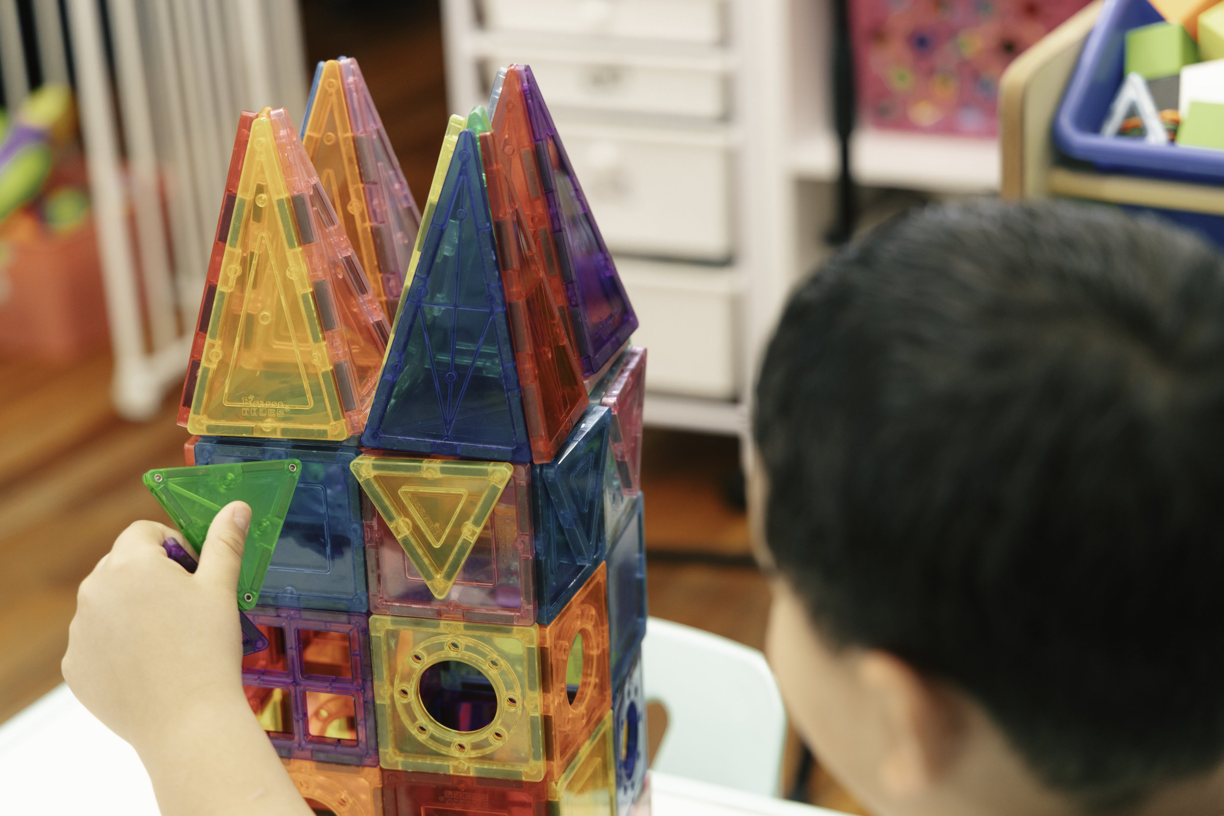 A child building a tower with colorful magnetic construction pieces indoors.