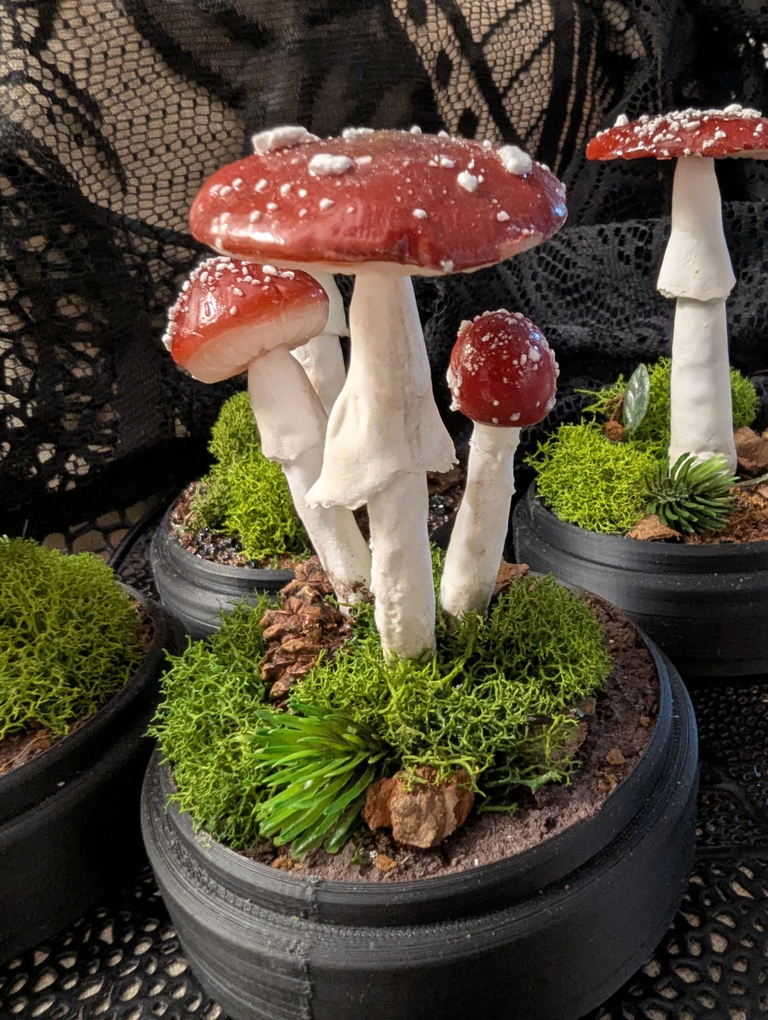 Artificial red-capped mushroom and moss decoration on a black pedestal.