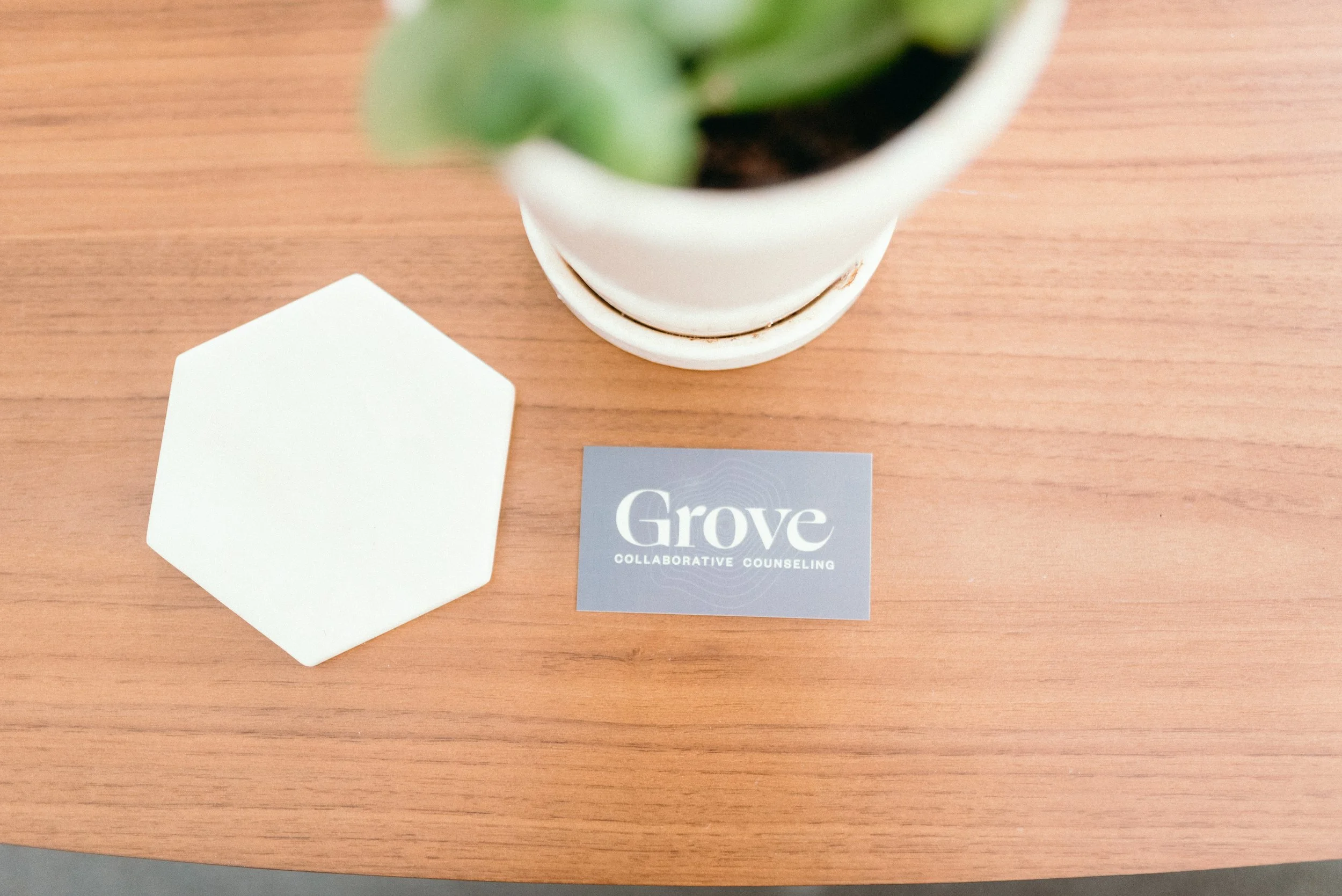 Photo of a coffee table with a white coaster, small green plant and business card that read Grove Collaborative Counseling.