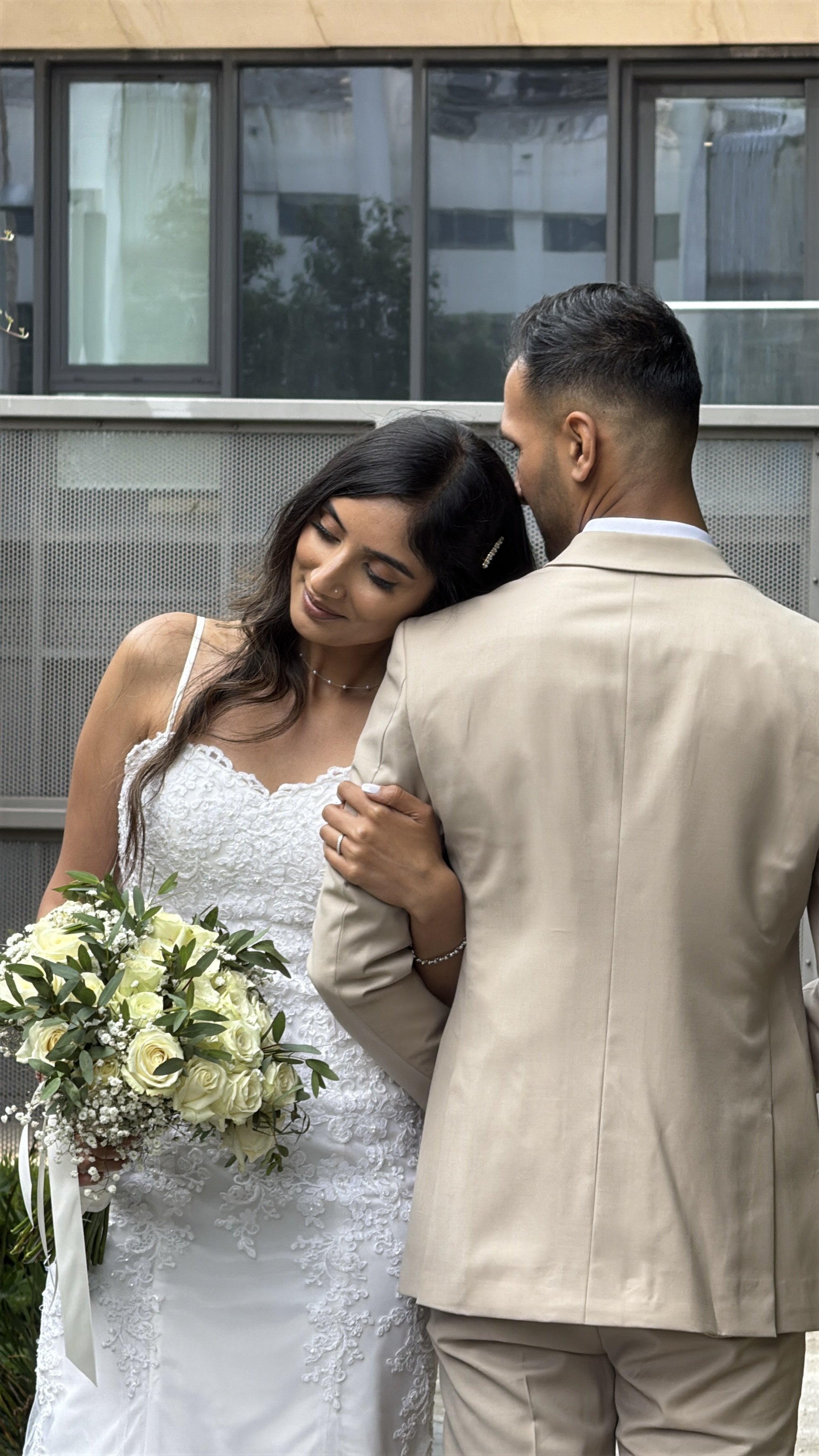 A bride and groom share an intimate moment, with the bride holding a bouquet and leaning her head on the groom's shoulder.