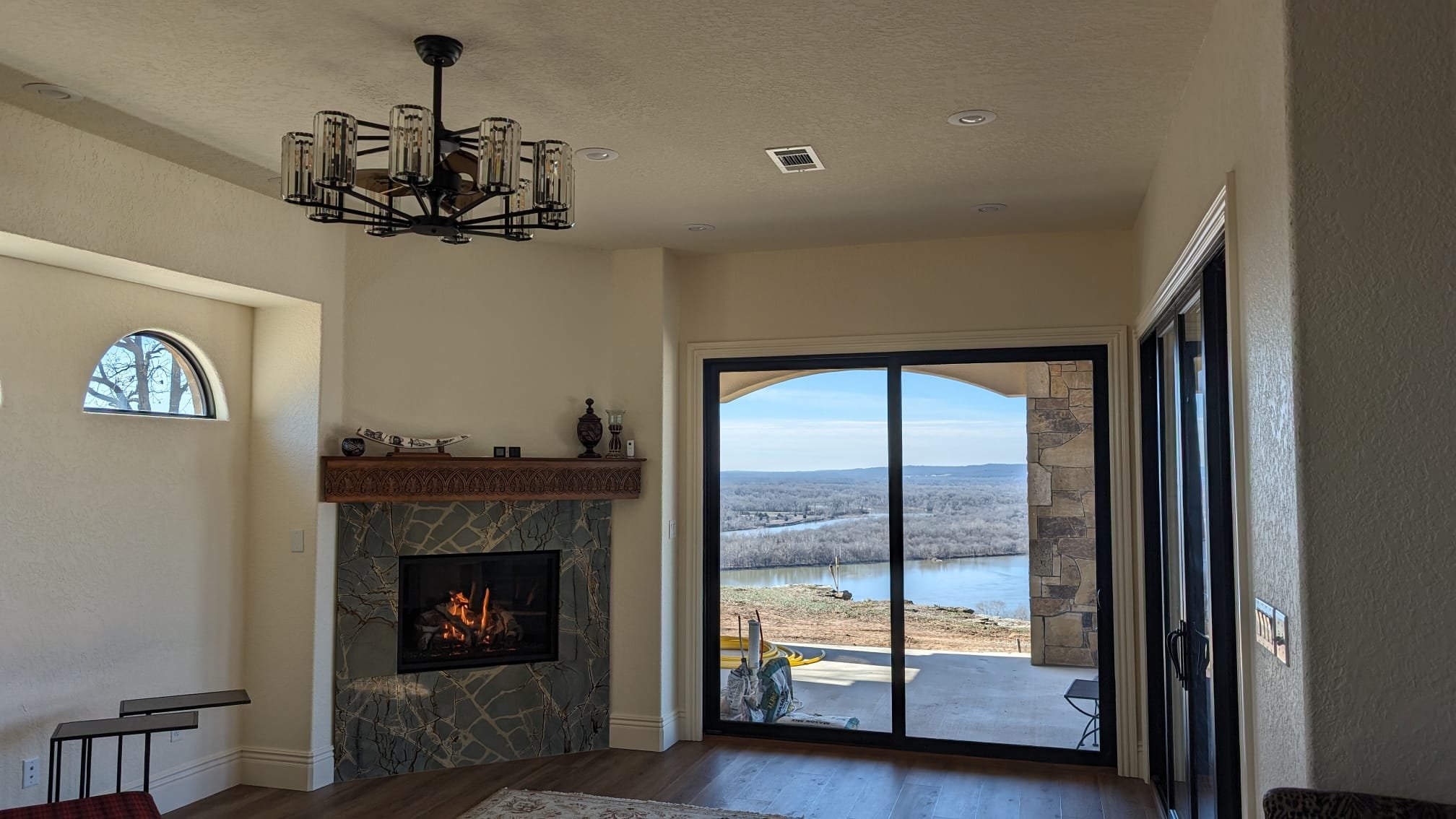 Living room with a fireplace, chandelier, sliding glass door showing a view of a river and trees outside.