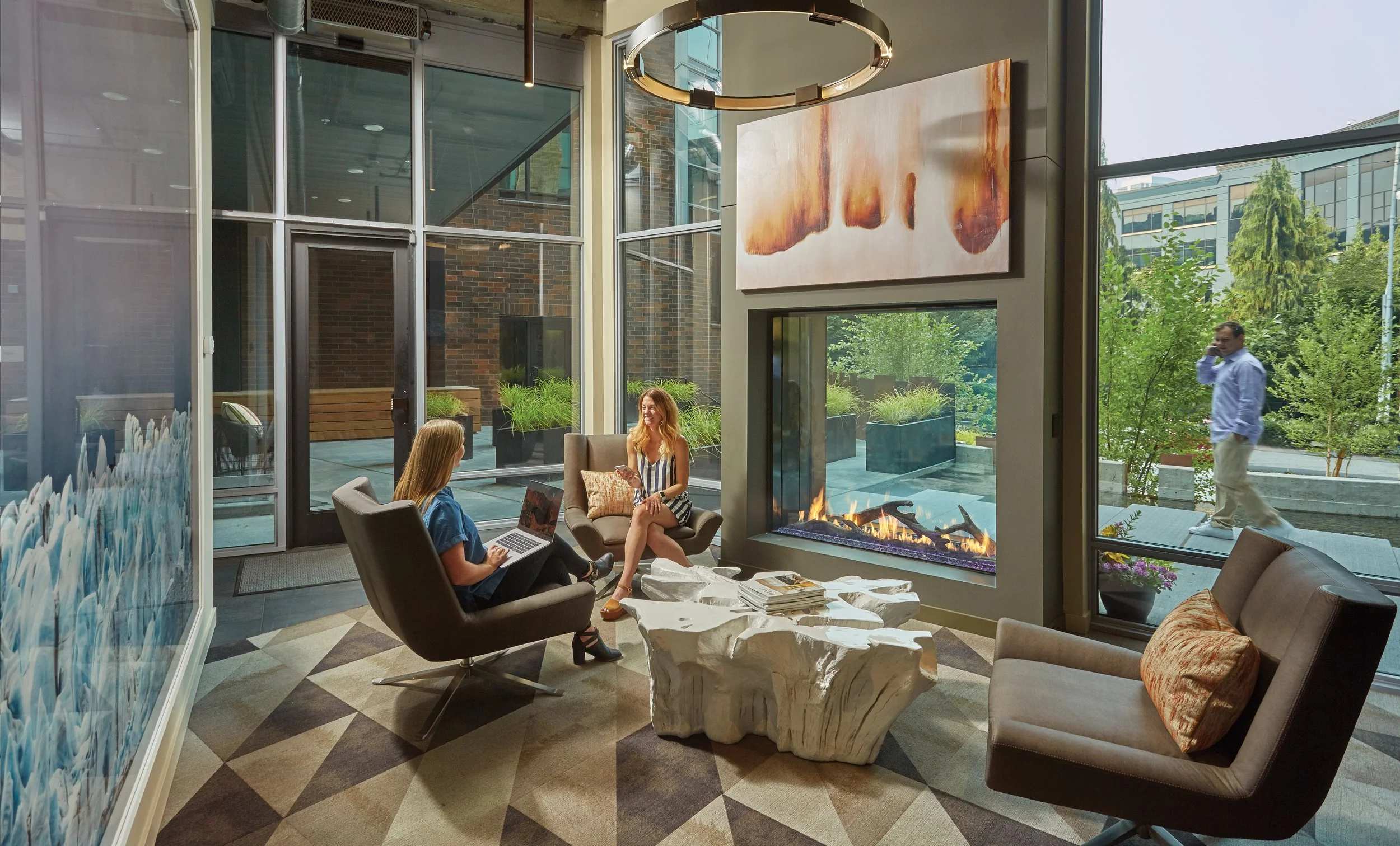 a see-thru fireplace in a glass space with two women having a meeting nearby
