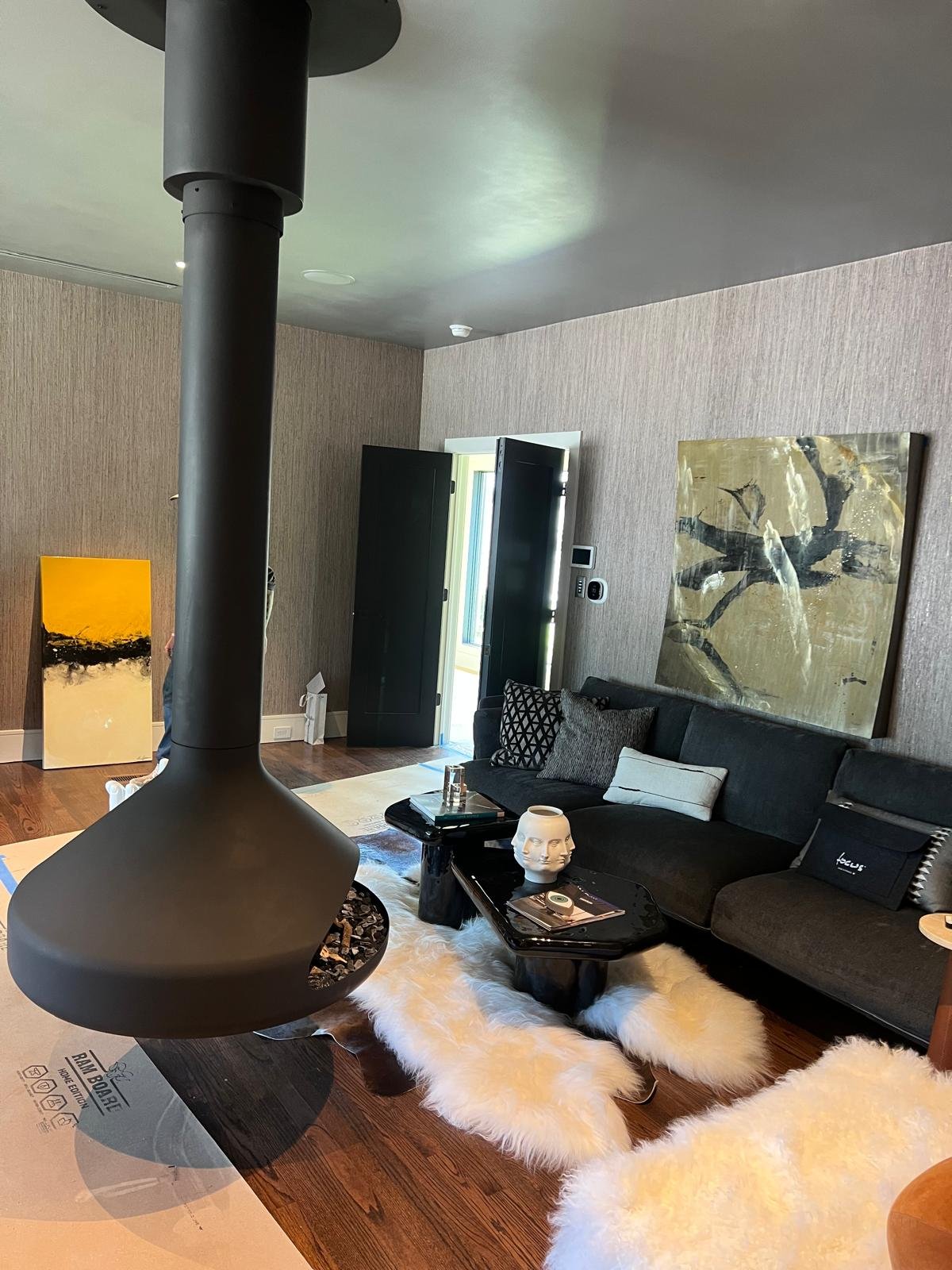 Living room with black sofa, artistic paintings, white fluffy rugs, coffee table with decor, and a black hanging fireplace.