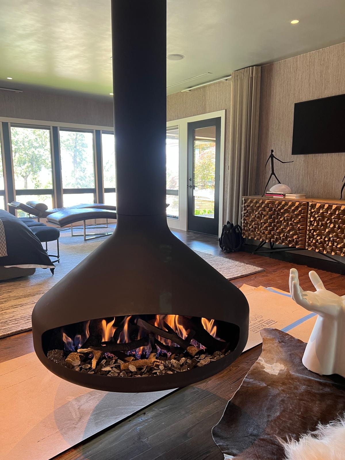 Modern living room with a black suspended fireplace, large windows, and contemporary furniture.