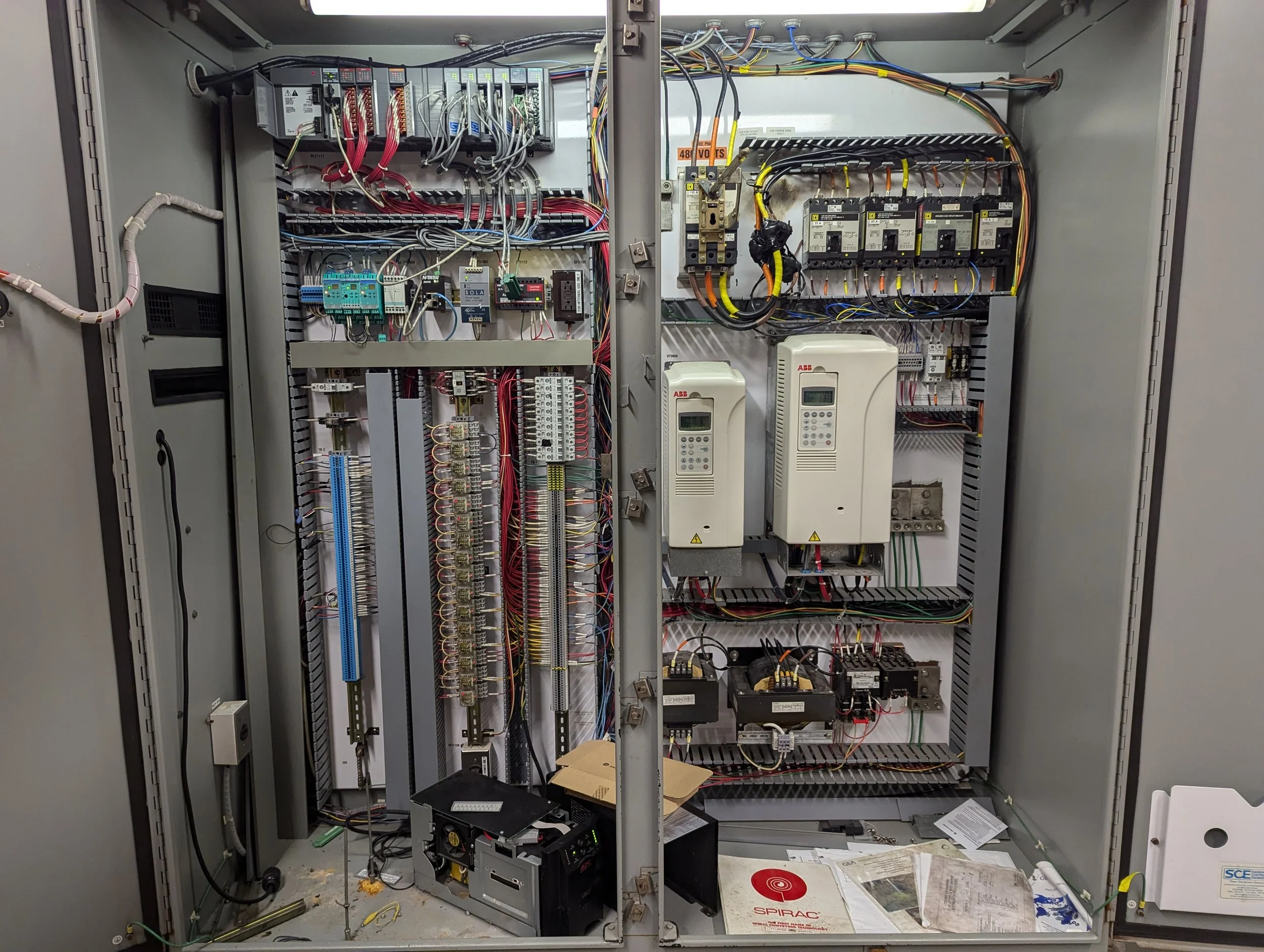 Open electrical control panel with various wires, circuit boards, and industrial components inside.