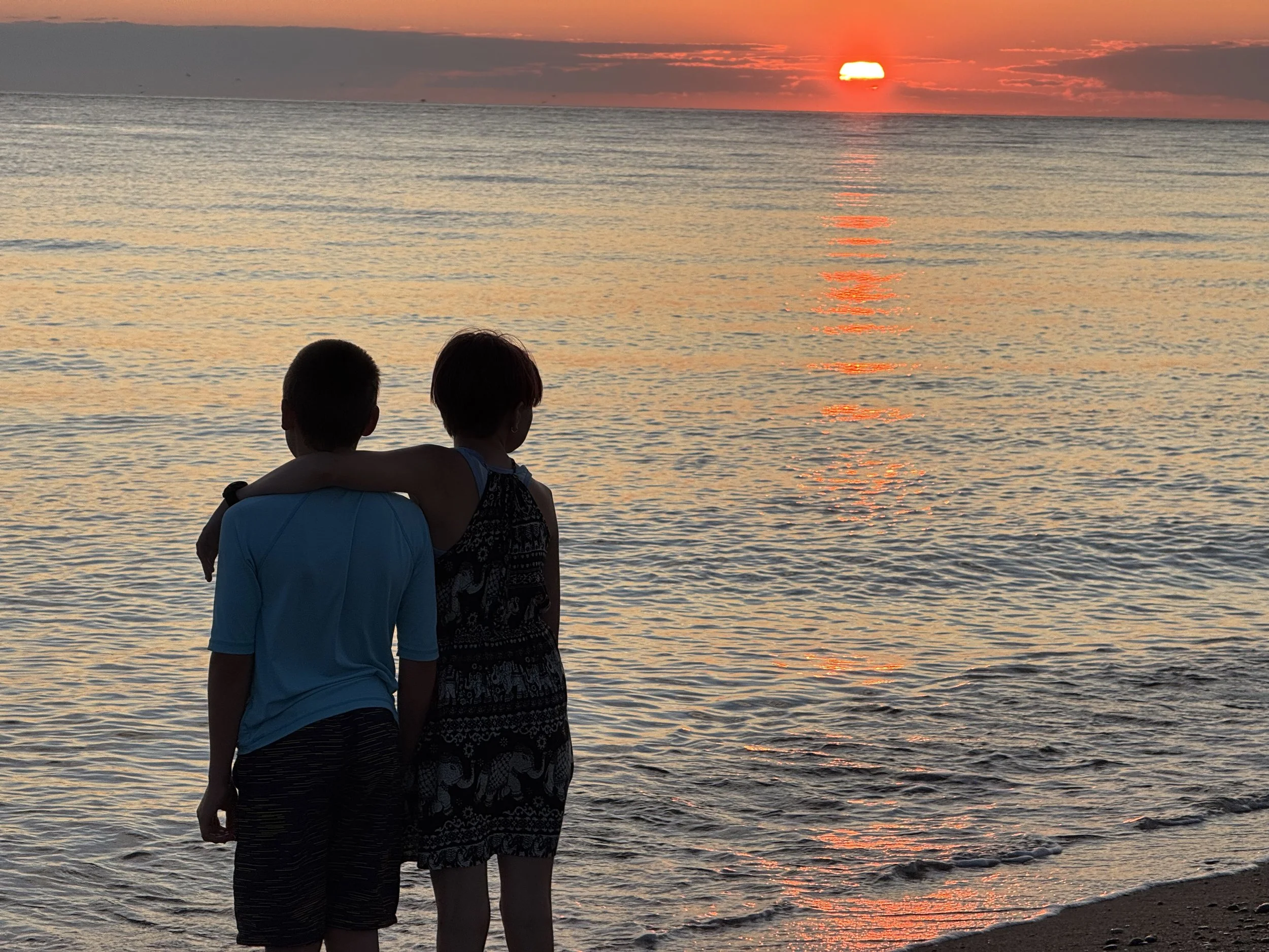 two tweens on the beach looking out at the sunset over the water evoking safety, steadiness and surety
