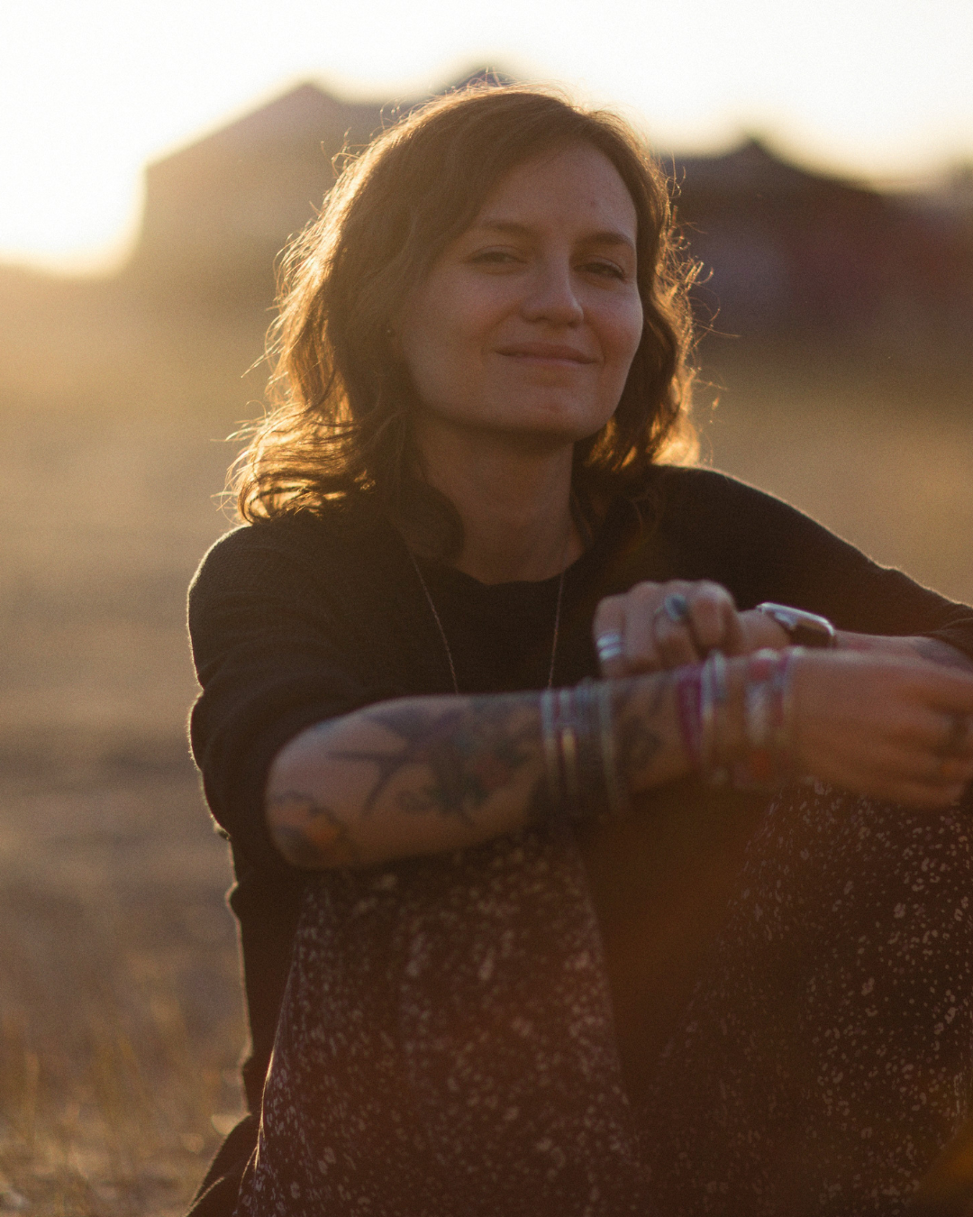 A woman with a relaxed smile, sitting outdoors during sunset.