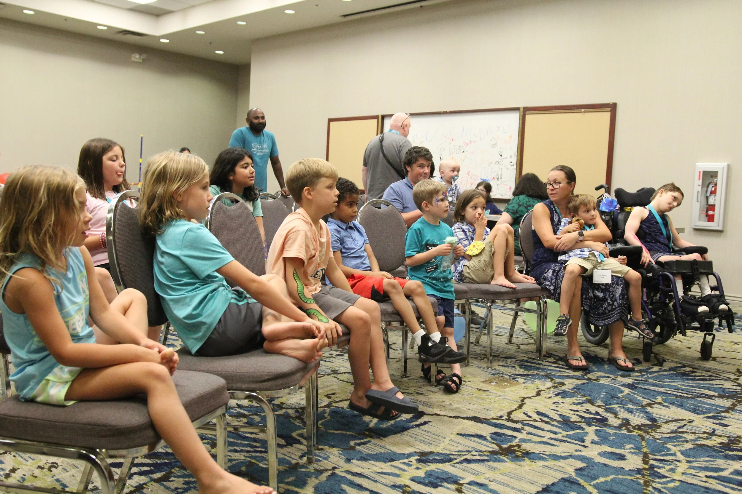 A number of children sit in chairs, facing a storyteller who is off screen and not pictured
