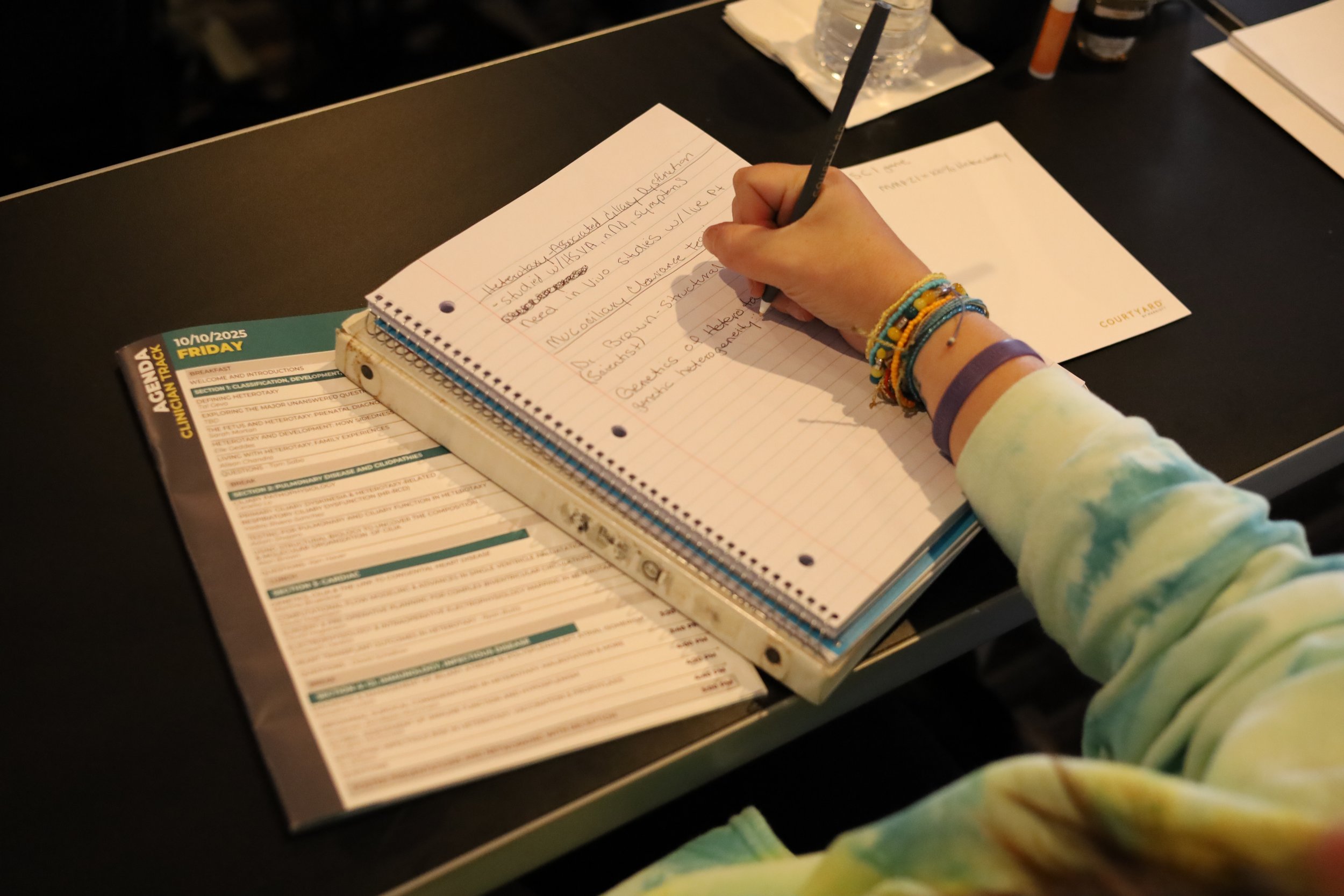 a hands is shown holding a pen and writing notes in a notebook with a conference agenda open next to the notebook