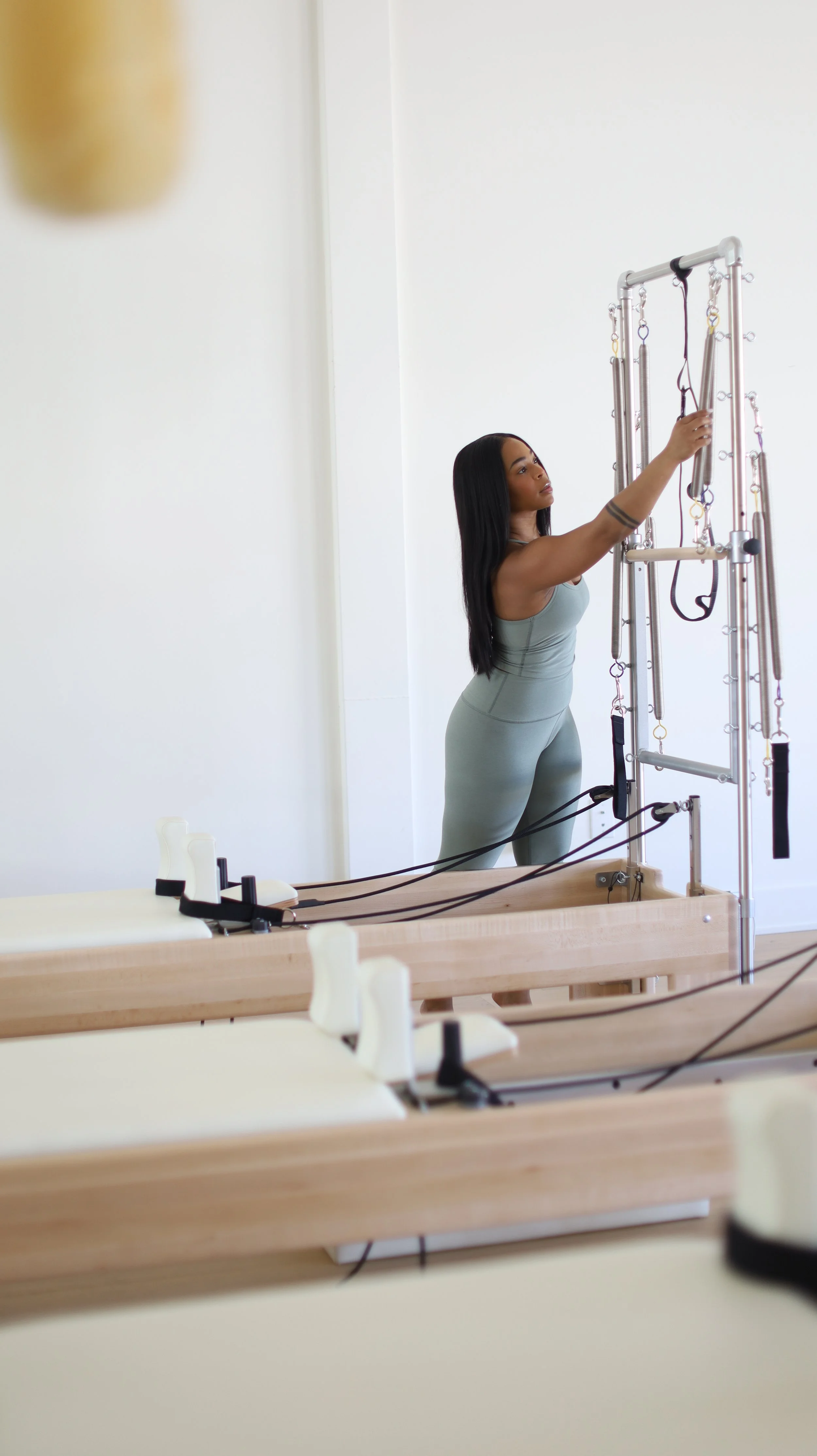 A woman in gray workout attire adjusting Pilates equipment in a studio.
