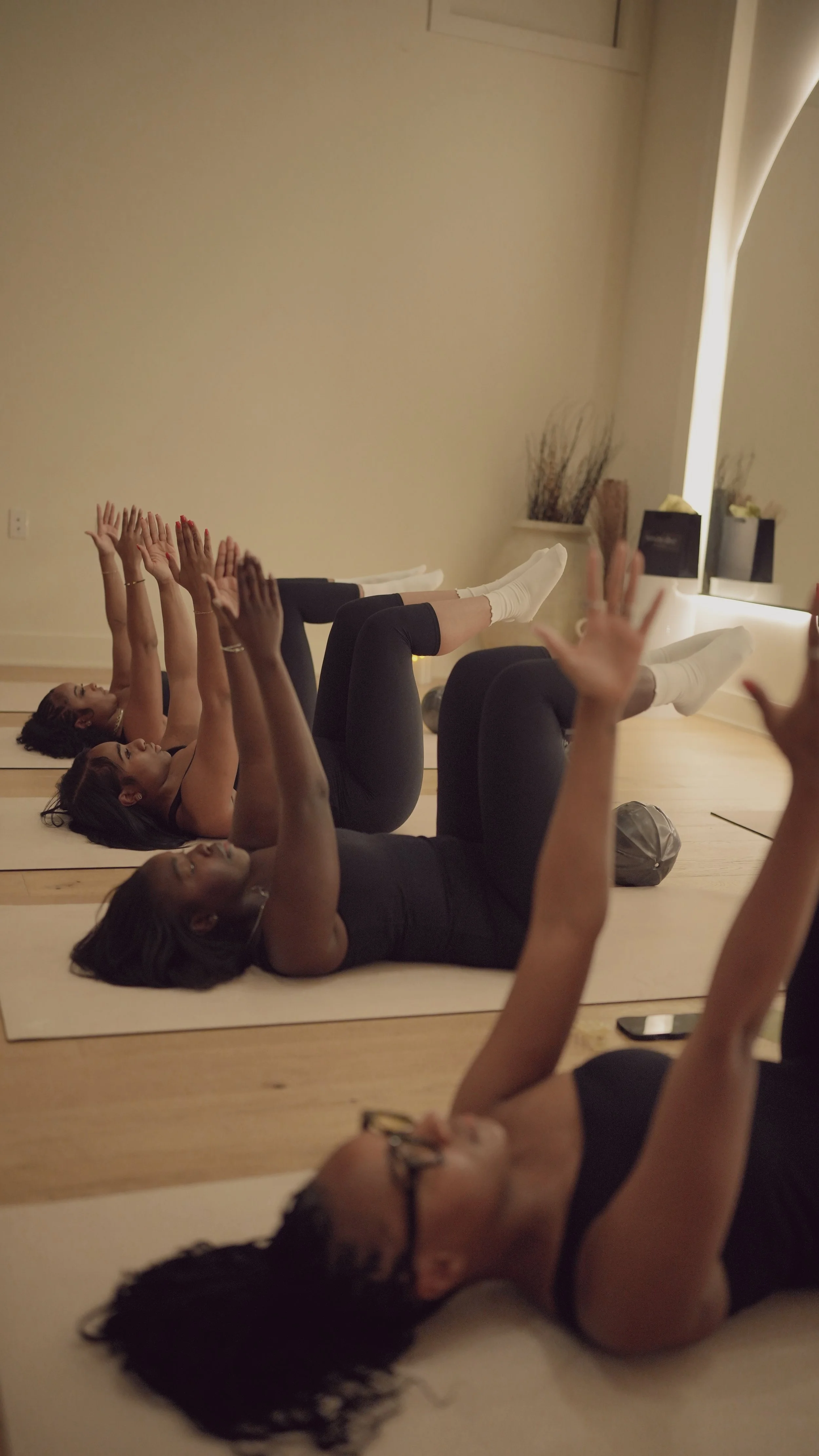 A pregnant woman practicing yoga indoors, stretching with one arm raised and holding her foot behind her, wearing a white sports bra and white leggings.