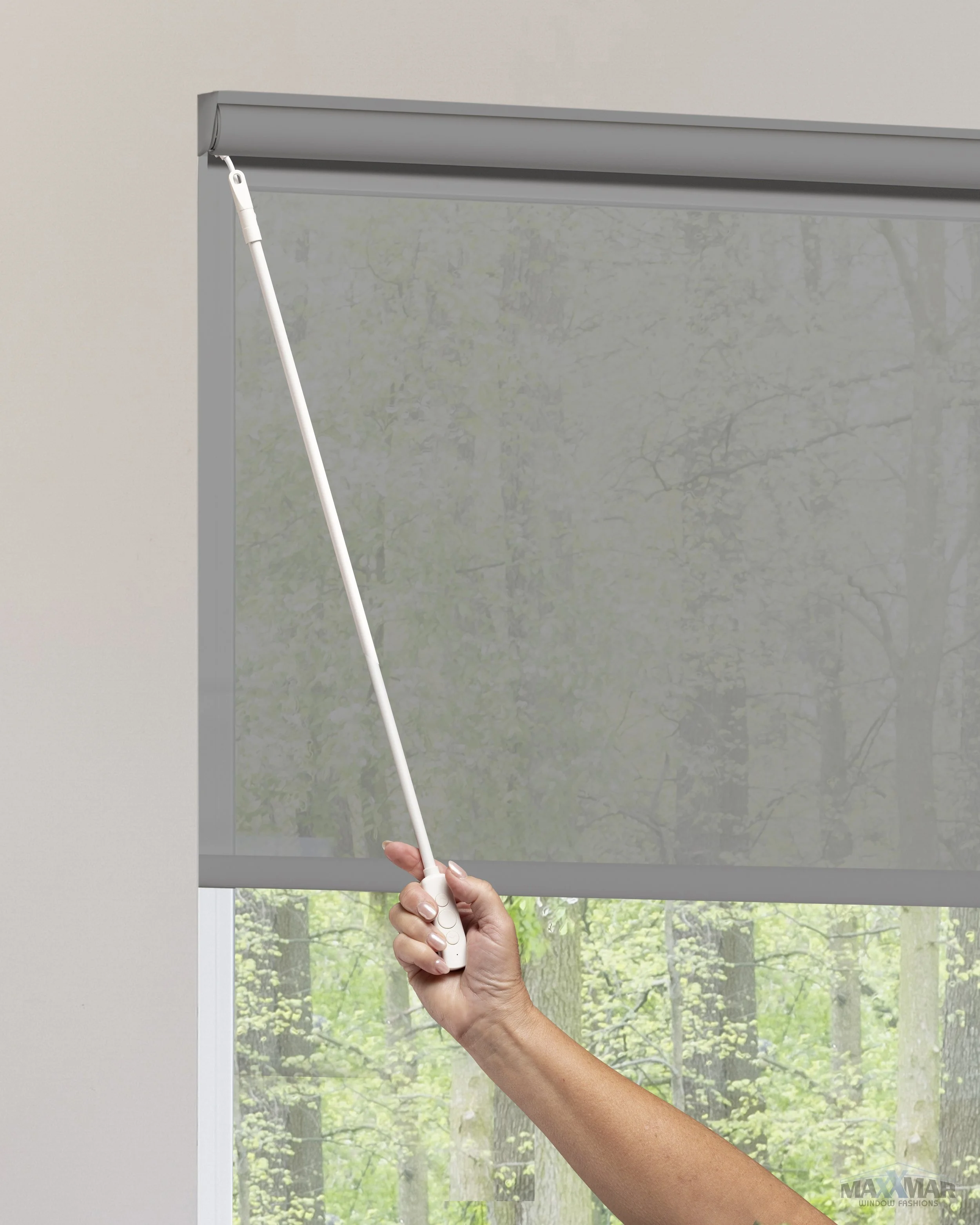 Hand lowering a window shade with a remote control.