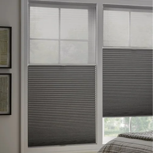Two large windows with gray horizontal blinds, partially open, in a bedroom with a bed and framed pictures on the wall.