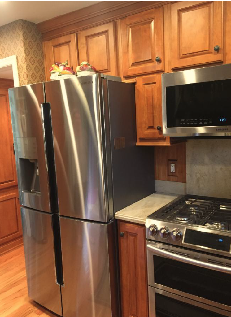 Stainless steel refrigerator next to a wooden kitchen cabinet, with a microwave oven above a gas stove and oven, in a kitchen with hardwood flooring.