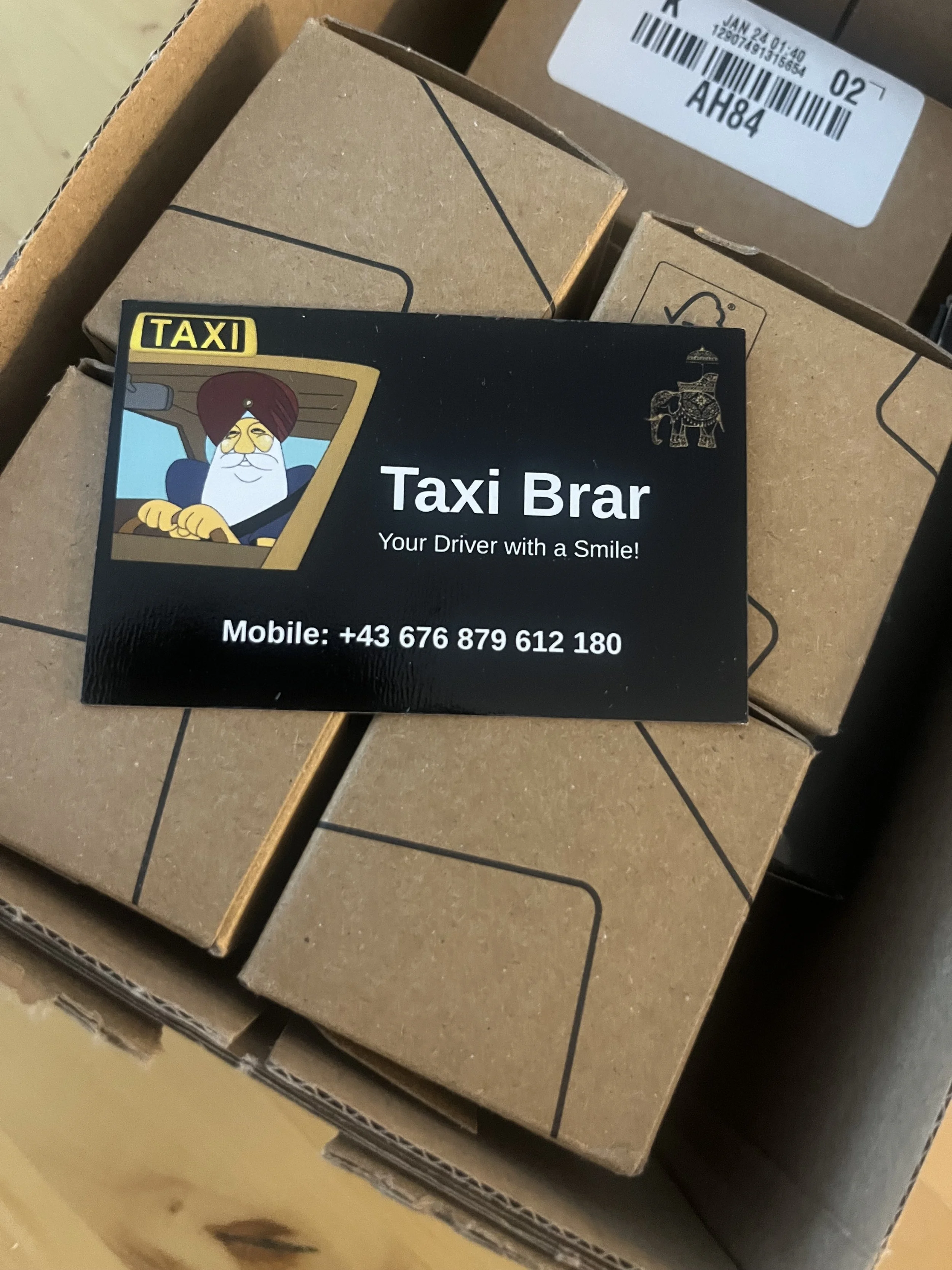 A business card for Taxi Brar, featuring a cartoon image of a smiling driver wearing a turban and glasses, with a mobile phone number +43 676 879 612 180.