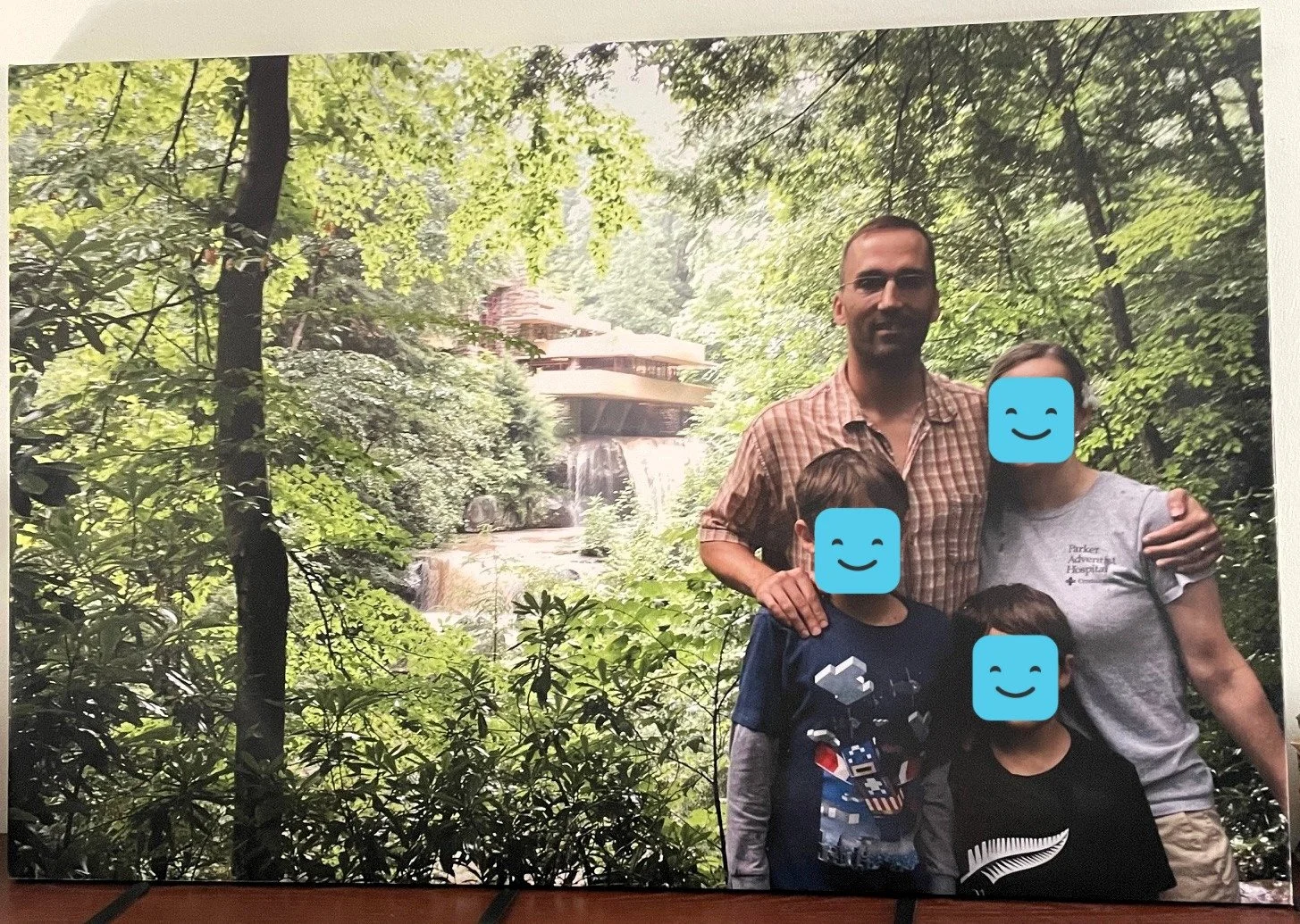 Family of four posed in front of a house situated over a waterfall, surrounded by a forest.