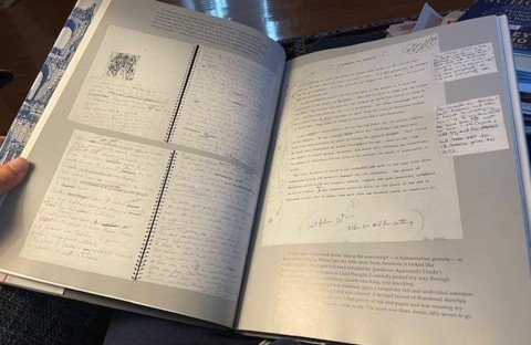 A two-page spread inside a large-format hardcover book, showing marked-up pages from the drafting of an earlier version.