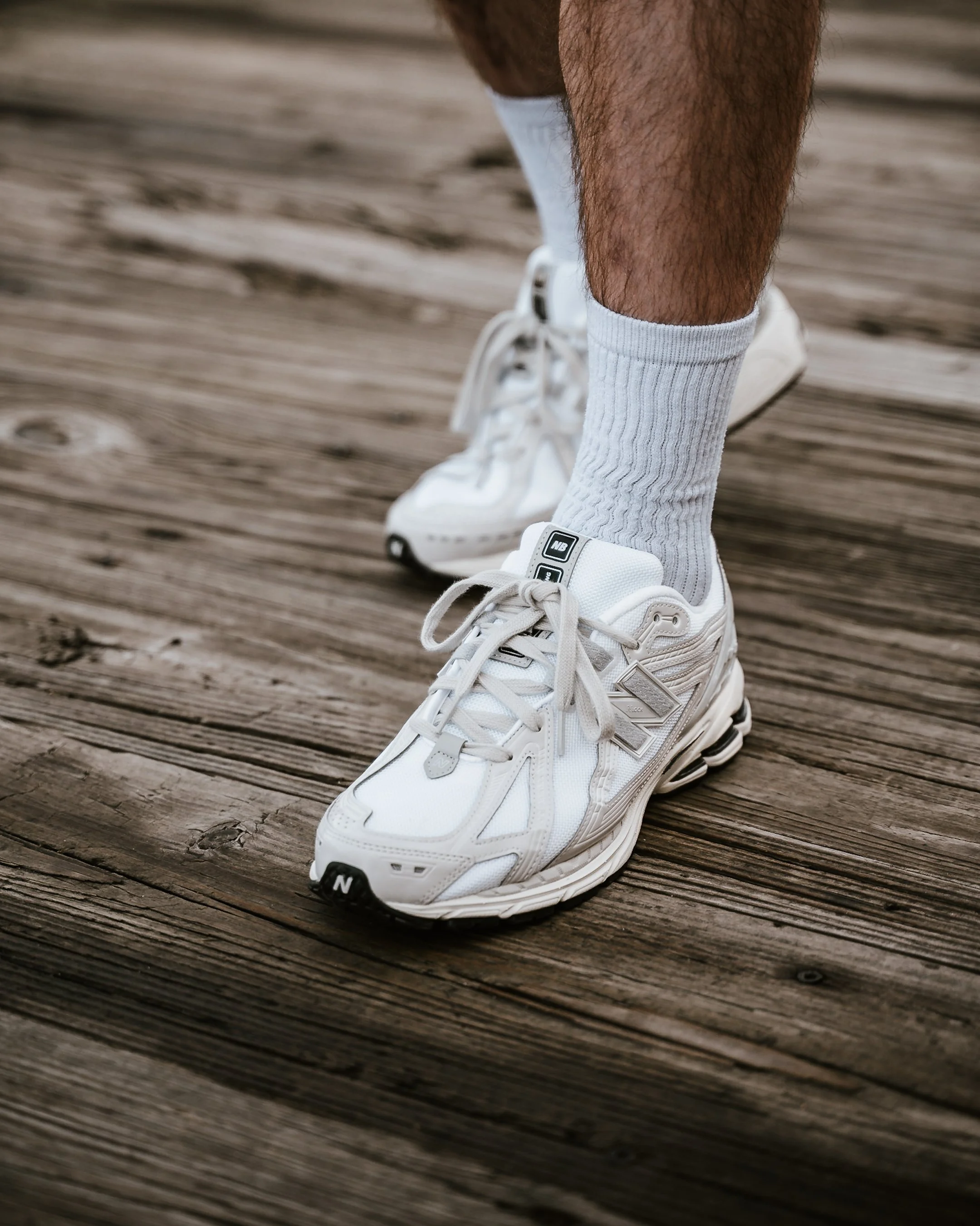 Close-up of a person's feet wearing white sneakers and white ribbed socks, standing on a wooden dock.