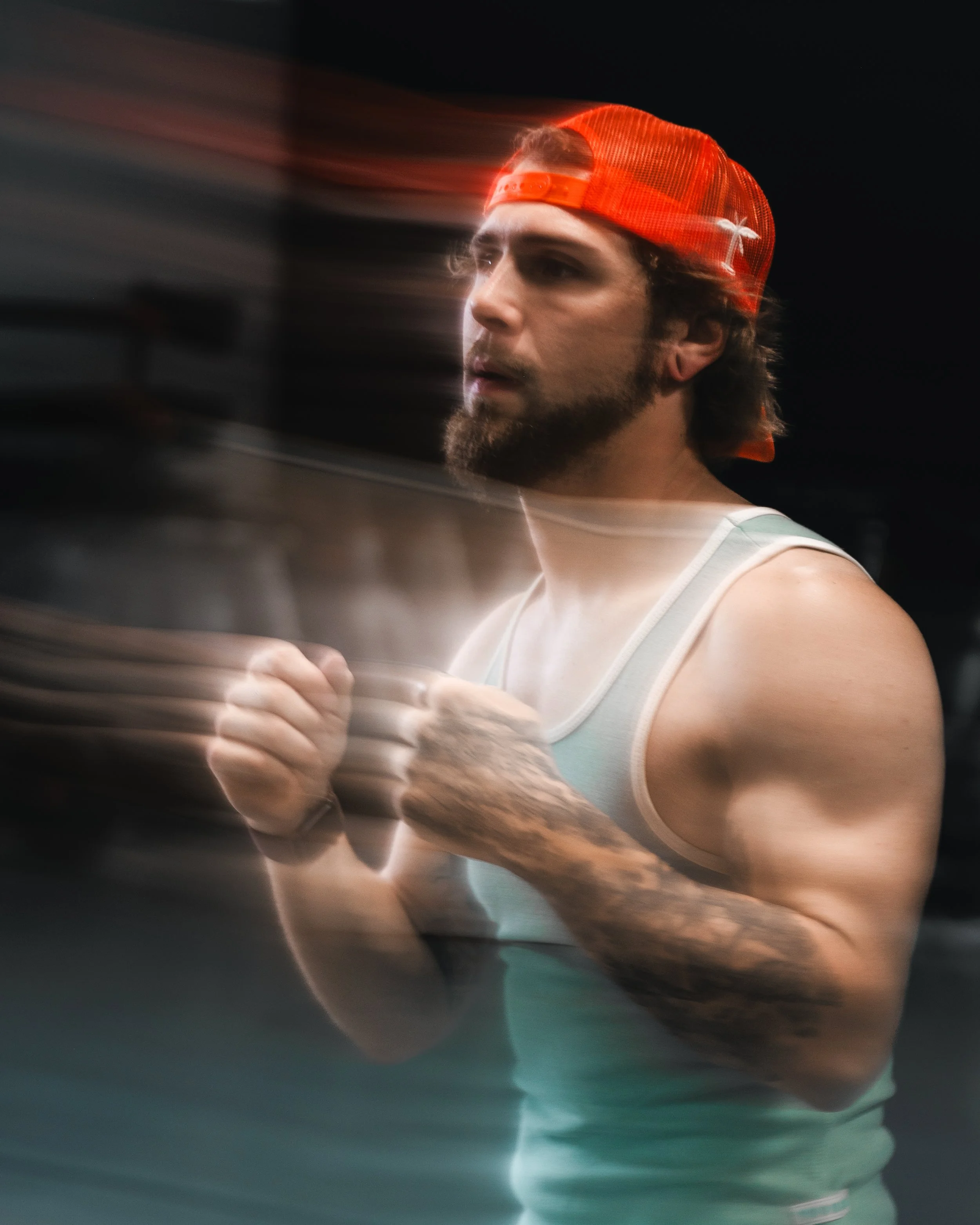 A man, wearing a red baseball cap backwards and a sleeveless shirt, appears to be running or jogging in a gym or indoor workout space.