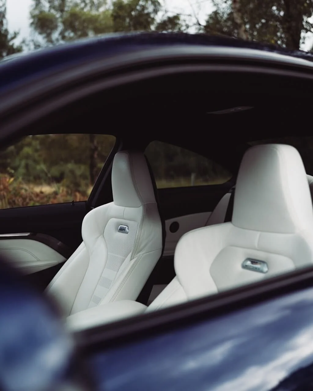 Front white leather seats inside a modern car, viewed through the car window with a blurred outdoor background.