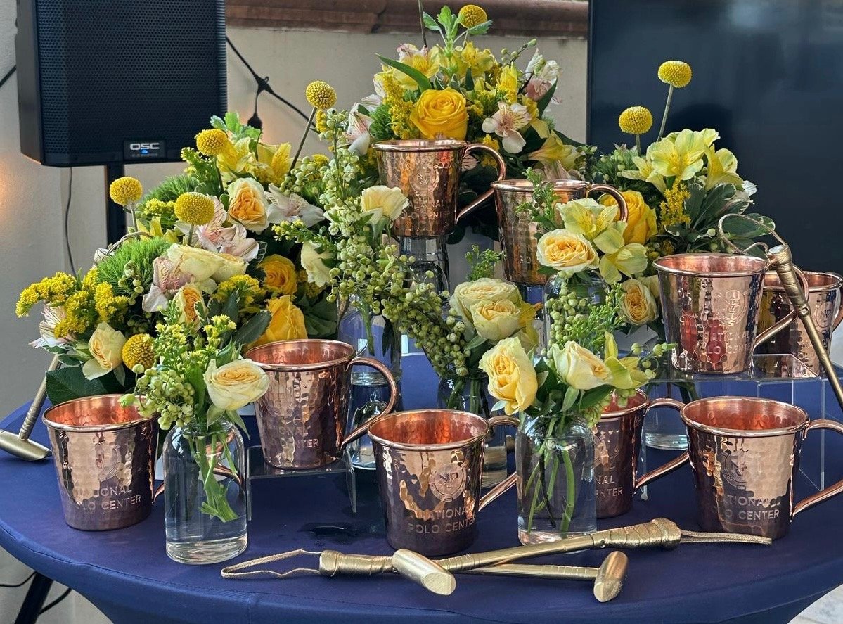 Vases with yellow and white flowers and copper-colored cups on a table with a blue tablecloth, with medical instruments in front.