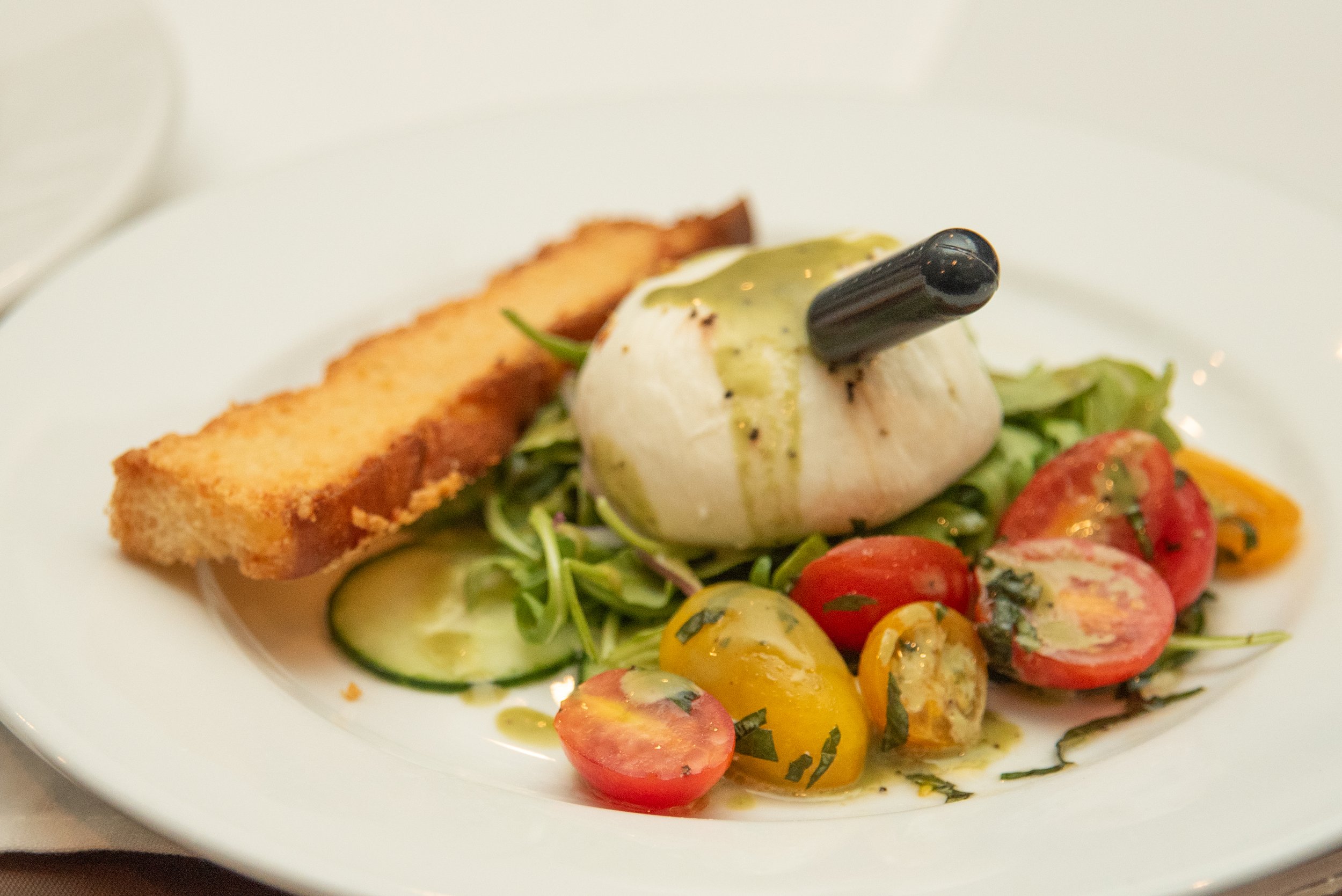 Caprese salad with cherry tomatoes, fresh basil, mozzarella, a black olive, and toasted bread slices on a white plate.