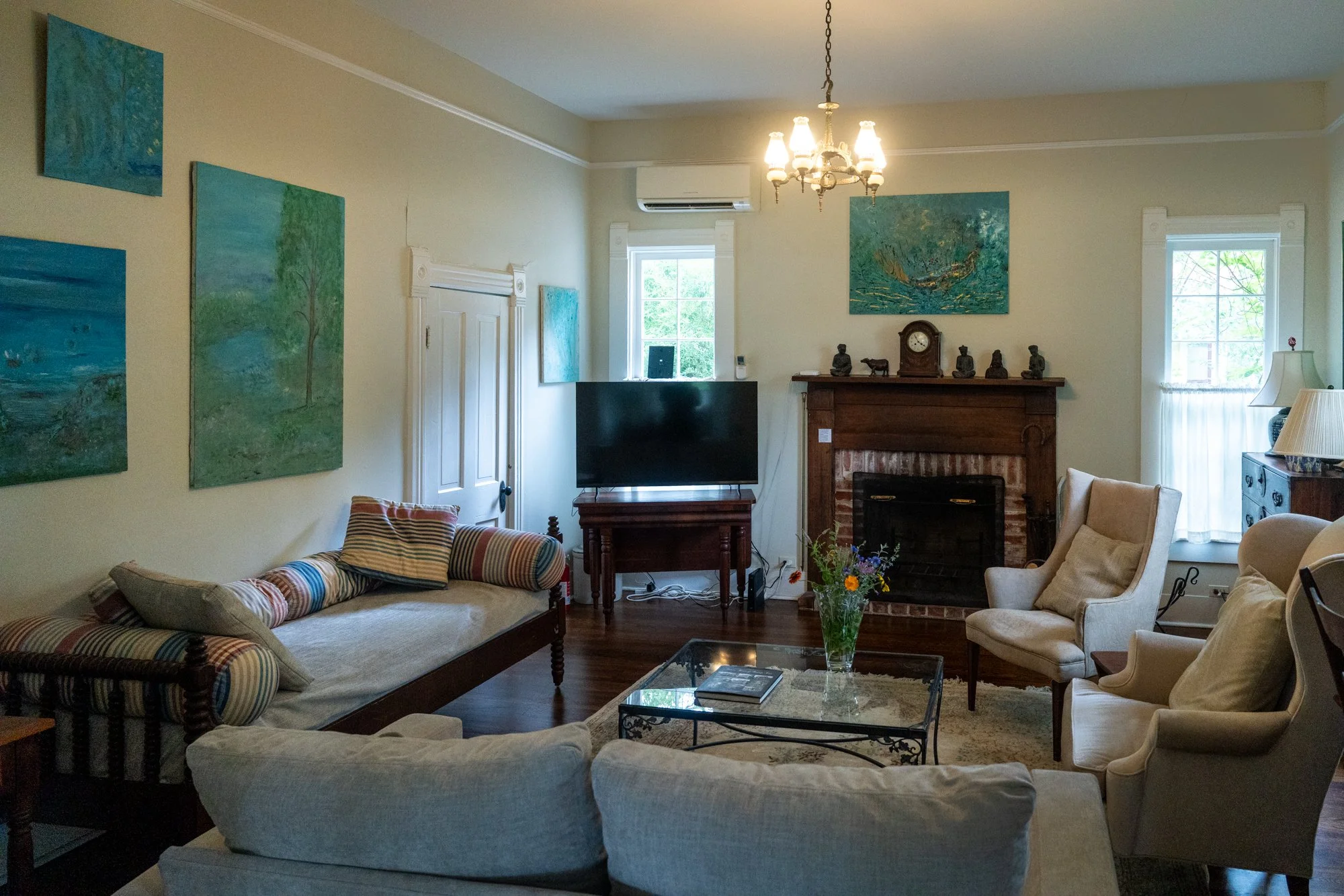 The living room includes a TV, daybed couch, wingback chairs, and a lovely working fireplace for intimate gatherings. The downstairs bathroom is accessible via the pictured door, and the room can be closed off with built-in sliding doors for privacy.