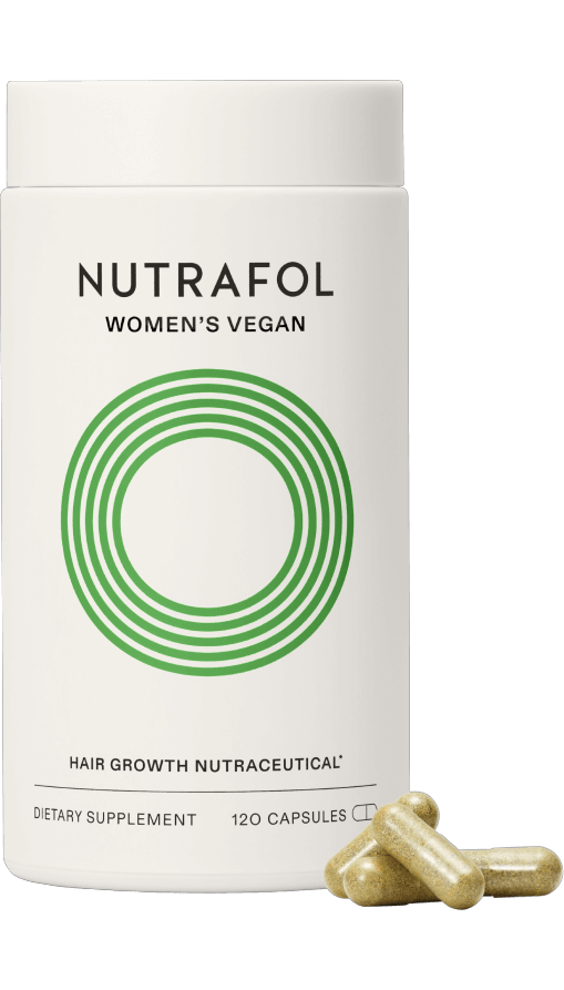 A white bottle of Nutrafol Women's Vegan Hair Growth Nutraceutical dietary supplement with three golden capsules in front of it on a black background.