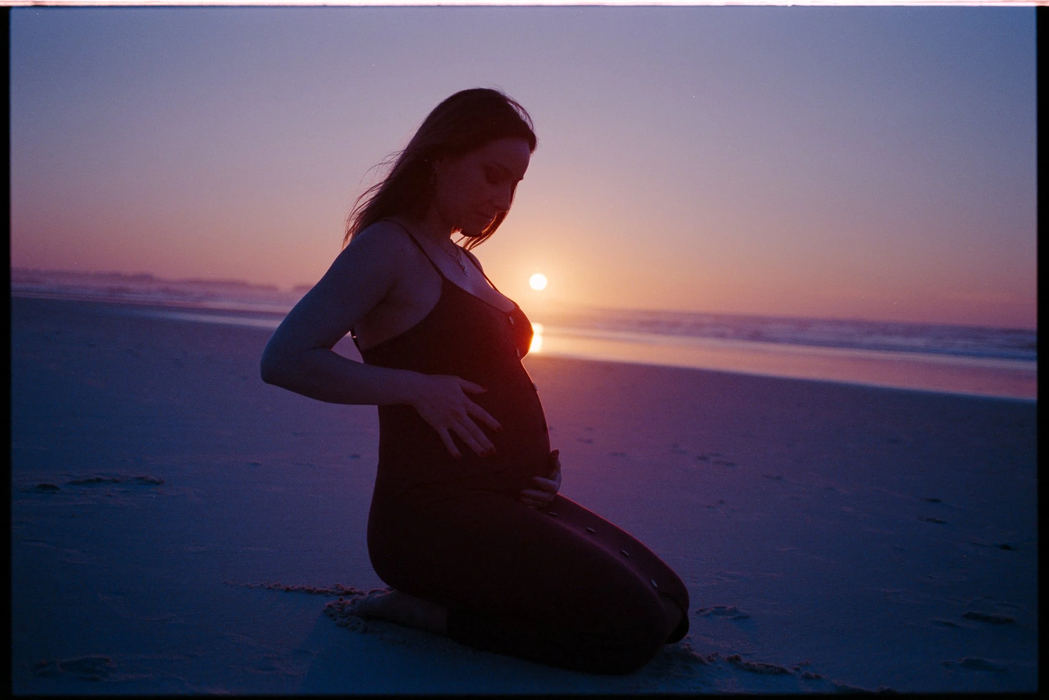 Pregnant woman on the beach at sunset holding her belly — maternity photo by Bruno Novais