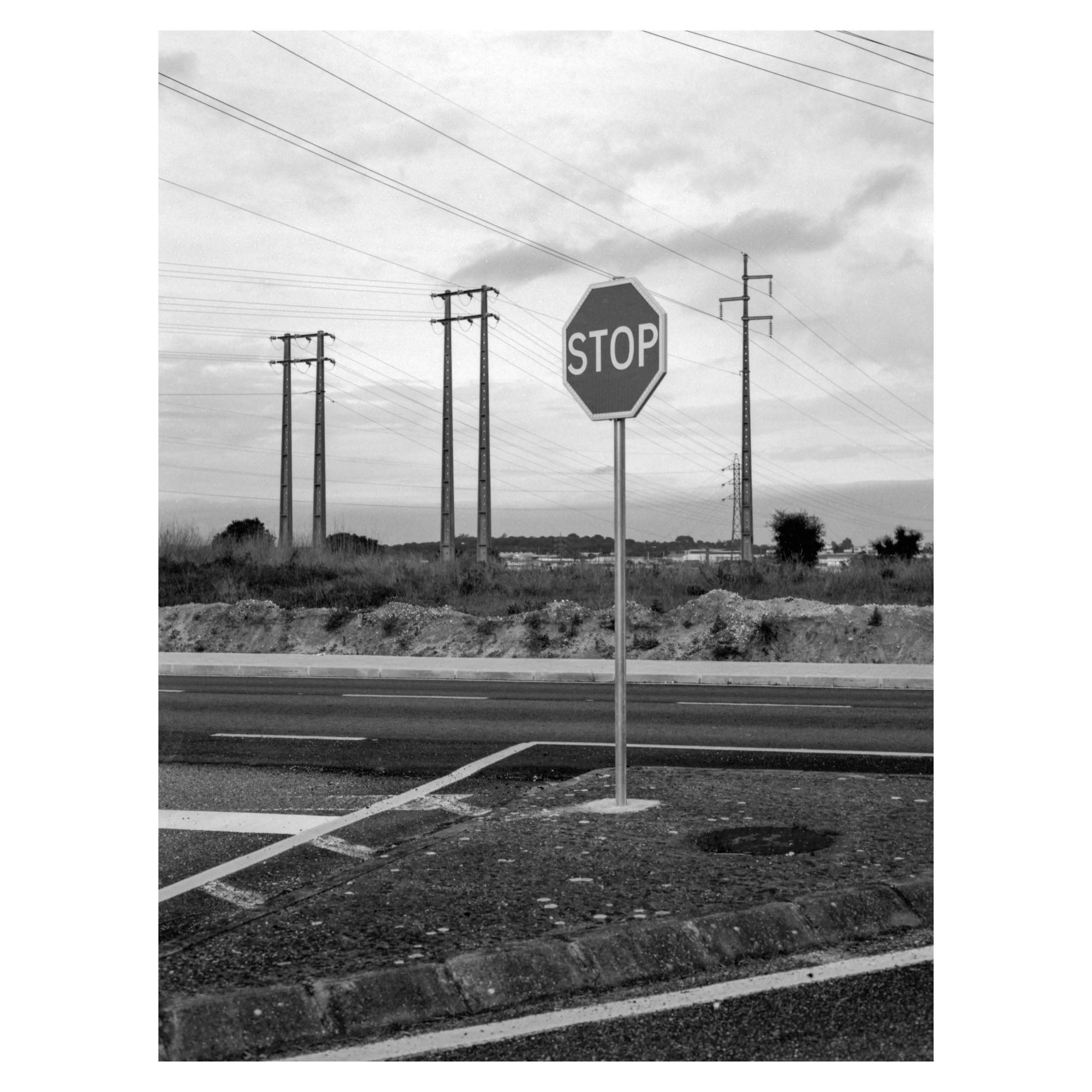 A stop sign on a road with power lines in the background, in black and white.