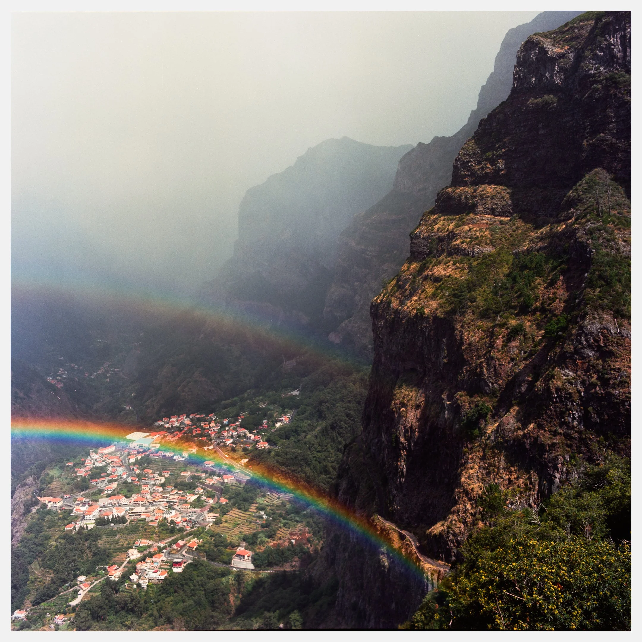 View of a mountain landscape with a small town below, and multiple rainbows arcing across the sky.
