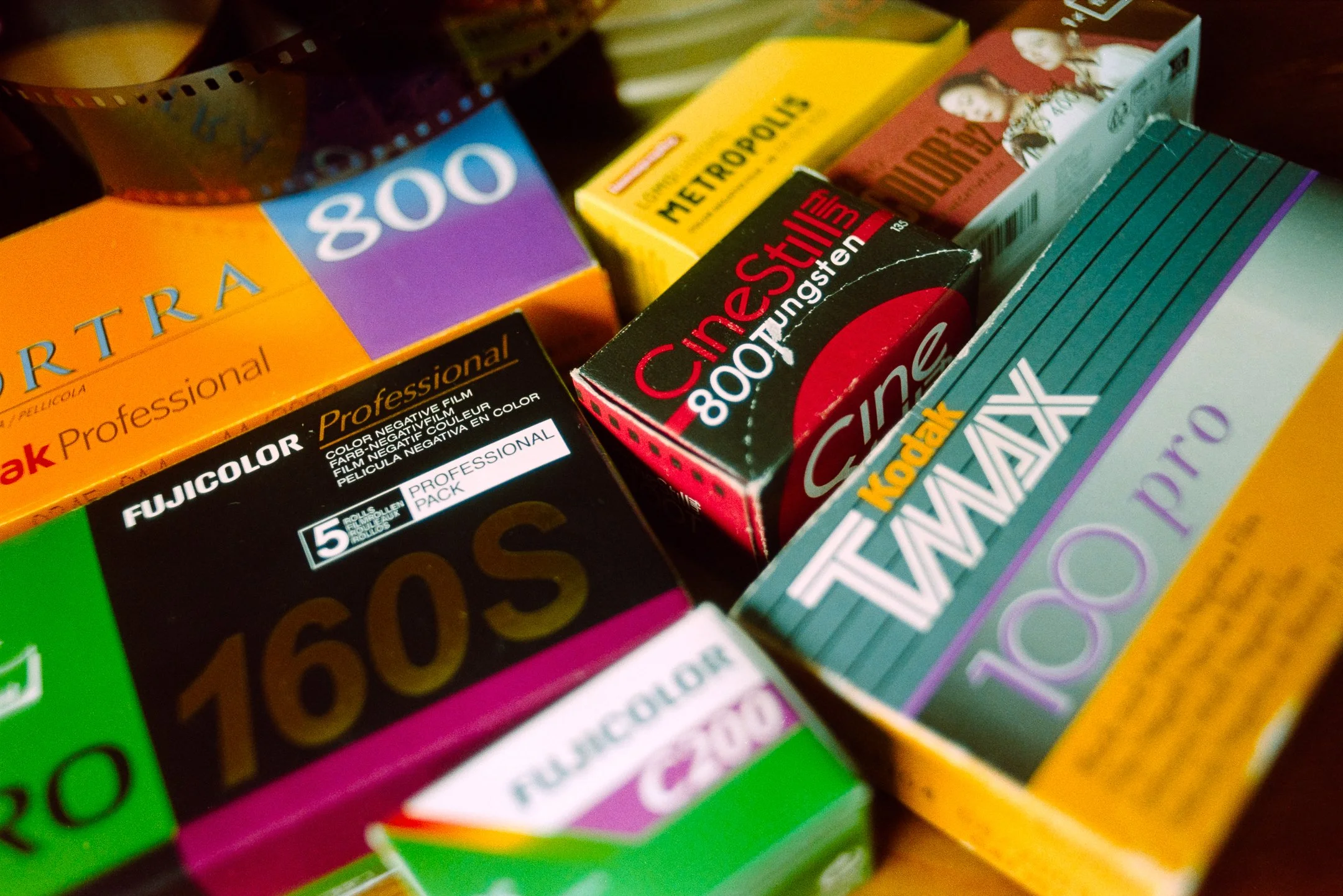 Close-up of various color film packs on a wooden surface, including Fujicolor, Cine Still, and Kodak Ultima.
