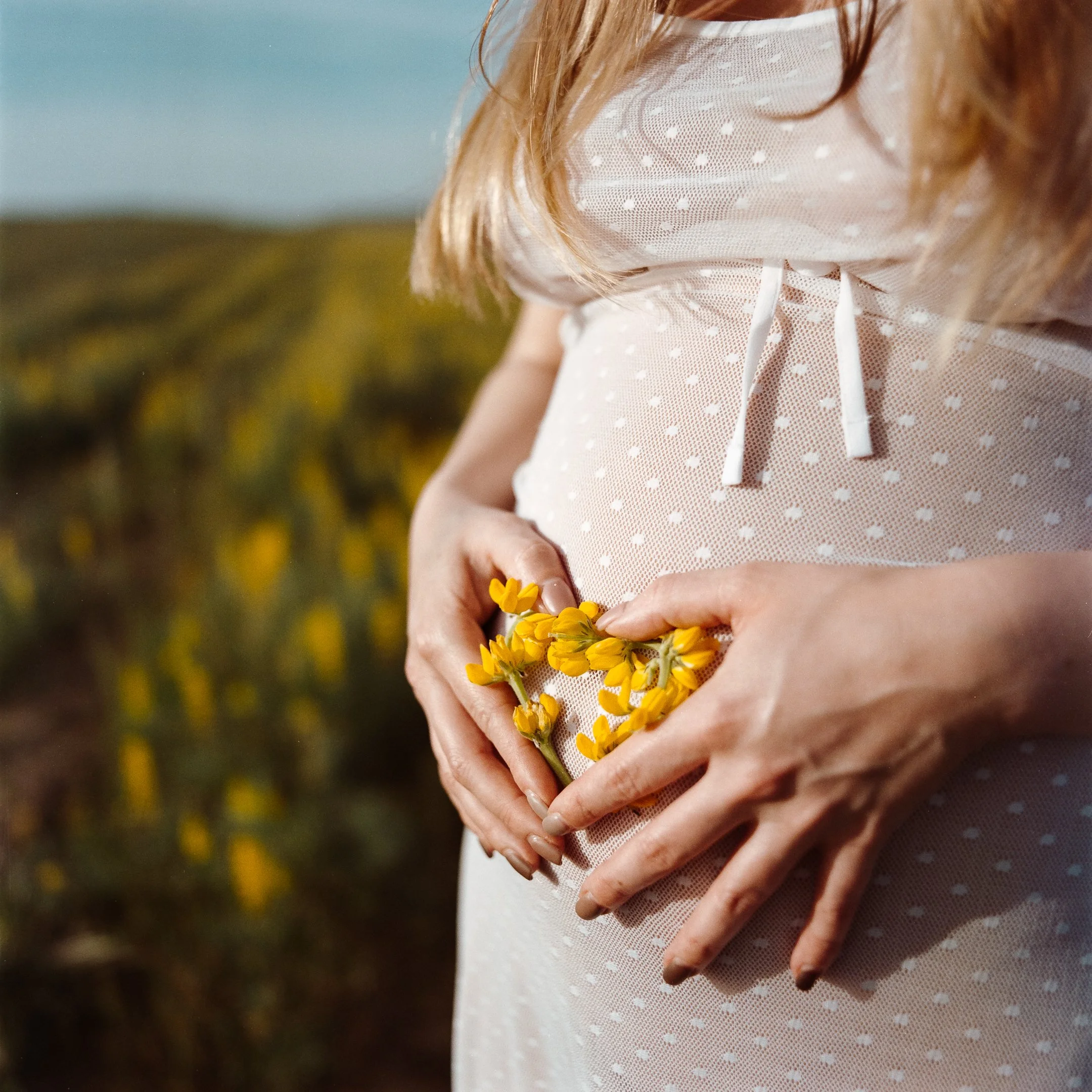 Pregnant woman holding a bunch of yellow flowers on her belly during daytime outdoor setting.