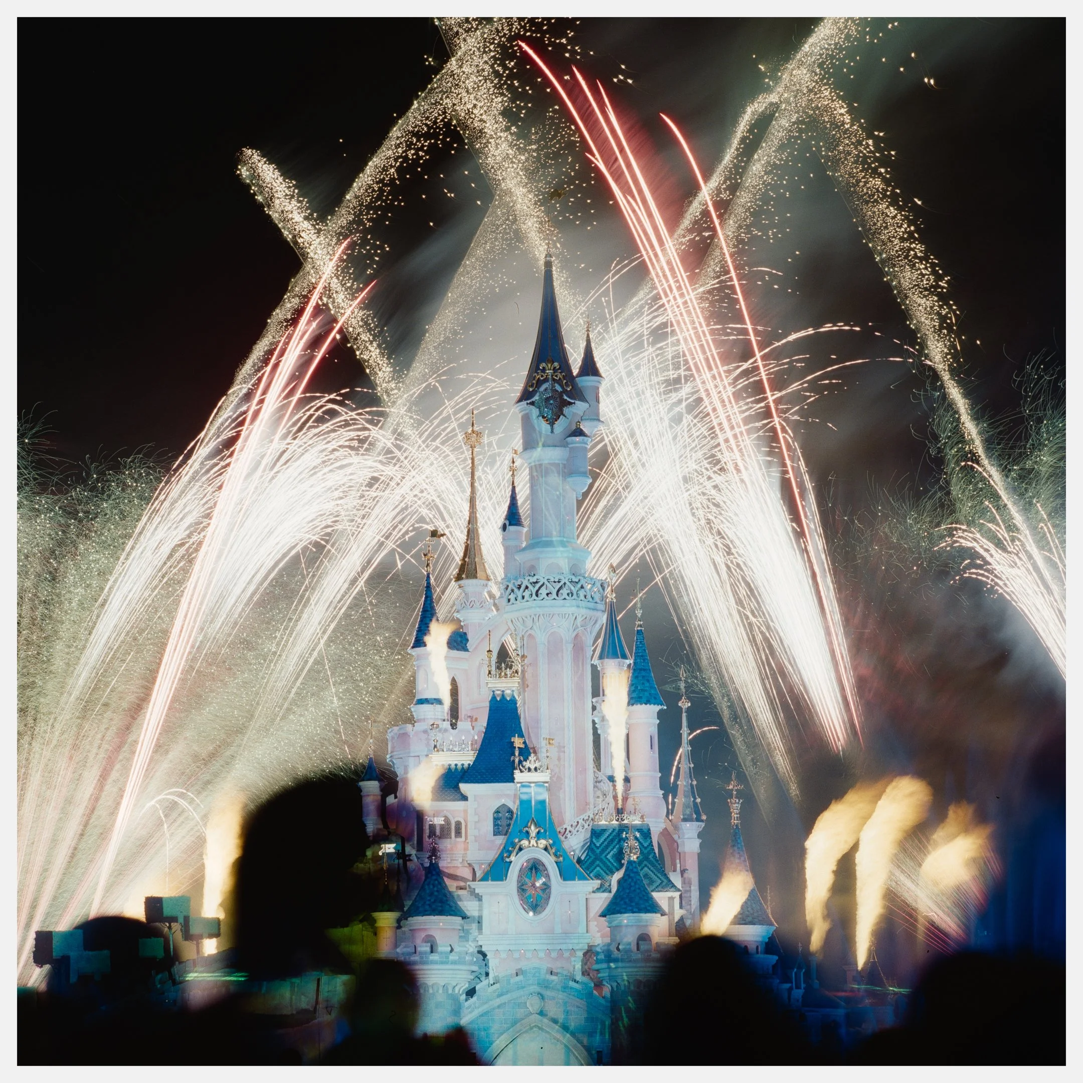 Nighttime fireworks explode around a castle at Disney theme park.