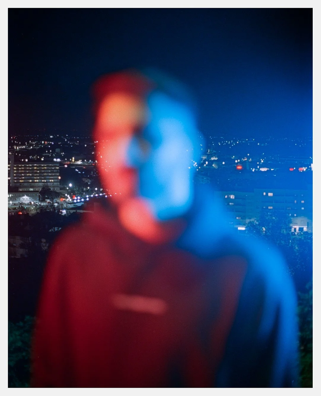 Blurred image of two people kissing with city lights in the background at night.